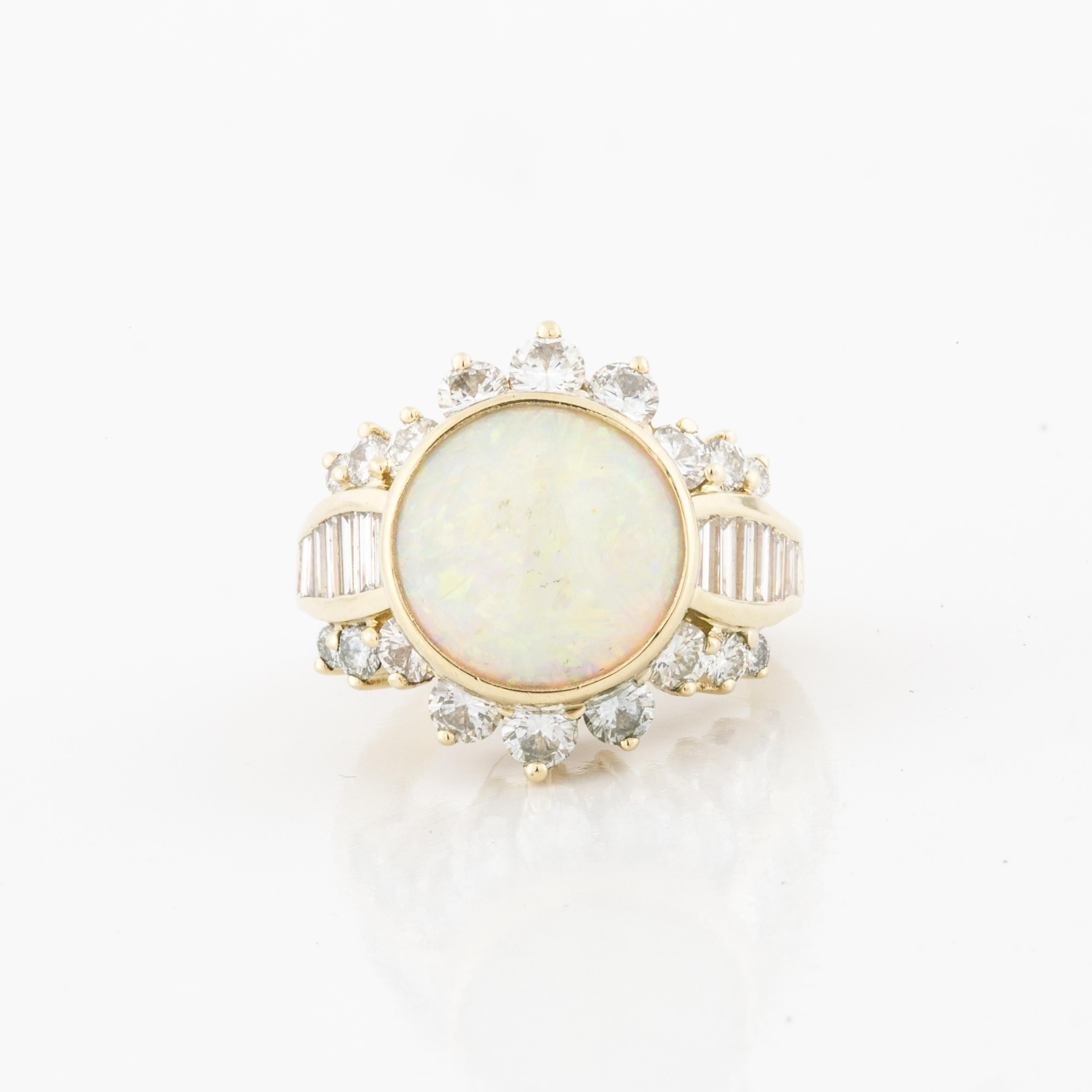 14K yellow gold ring featuring a round white opal accented by round and baguette diamonds. There are 18 round diamonds and 14 baguette diamonds that total 2.20 carats; H-I color and VS1-VS2 clarity.  The presentation area measures 7/8 inches by