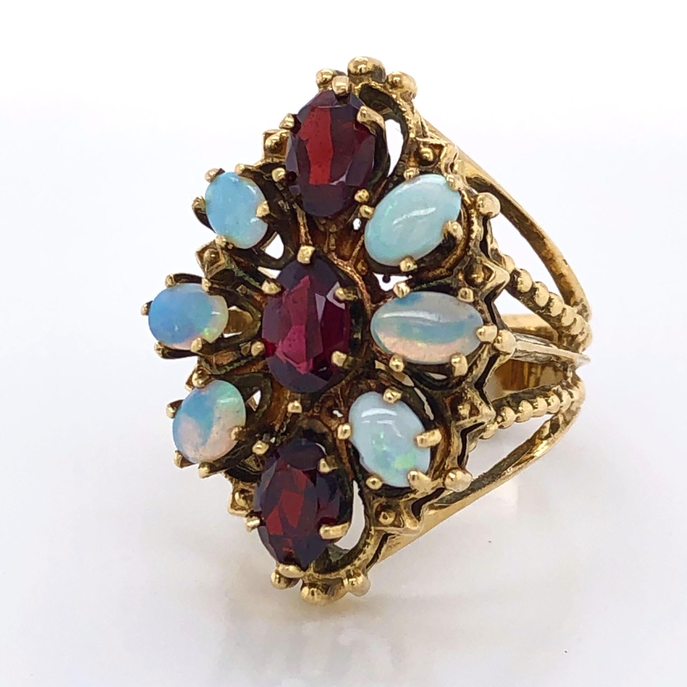 Six .03  carat fine natural opals artfully frame three .60 carat oval faceted-cut deep red garnets to create a colorful floral burst on this ornate cocktail ring. The gems stones are individually prong set and elegantly displayed in a fourteen karat