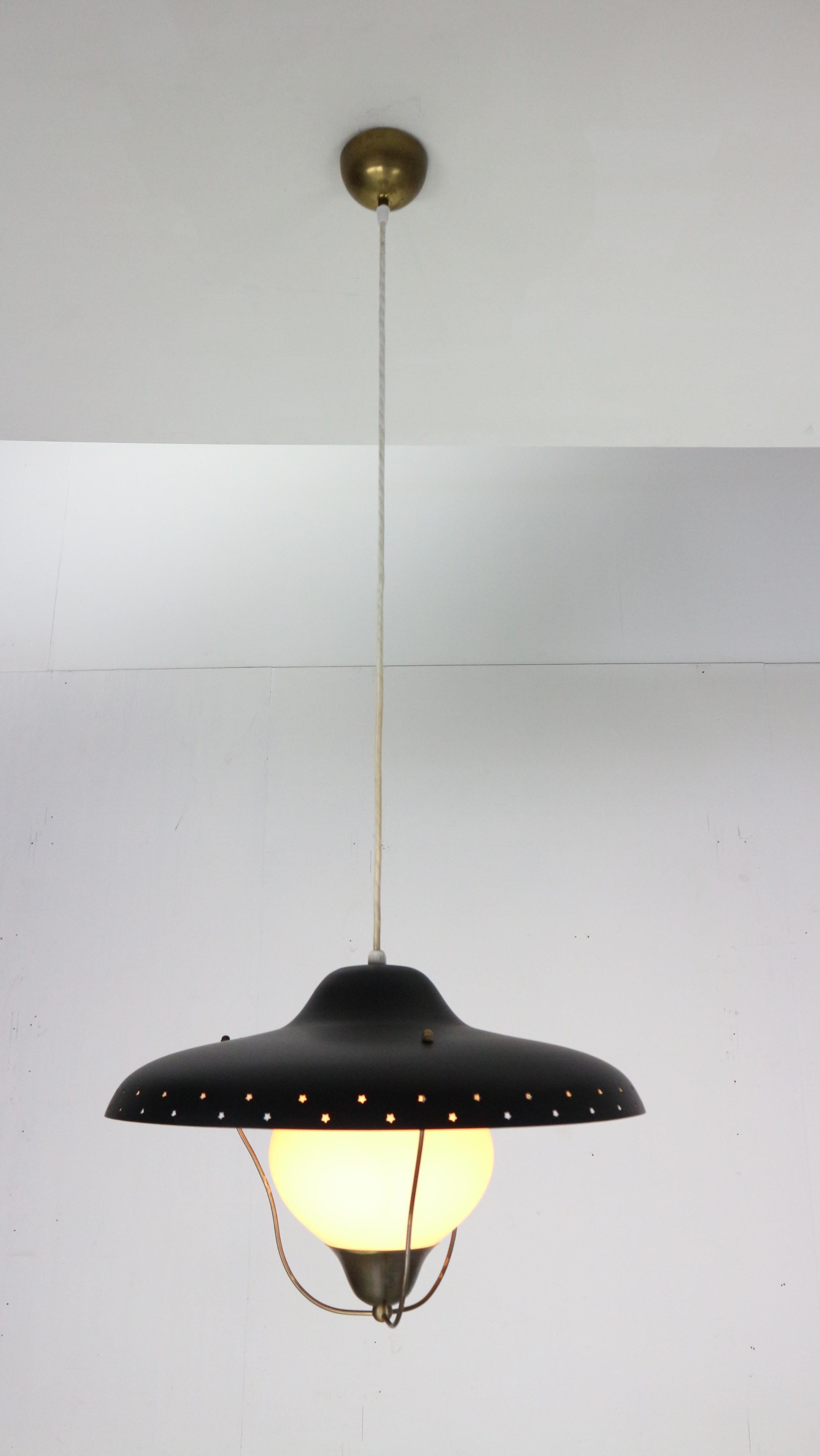 Pendentif en laiton, laqué noir et verre opalin conçu par Bent Karlby et produit par Lyfa, Danemark, années 1950. L'abat-jour présente des étoiles perforées et le verre est maintenu par une base en laiton.
La lampe mesure 25x45cm et est réglable en