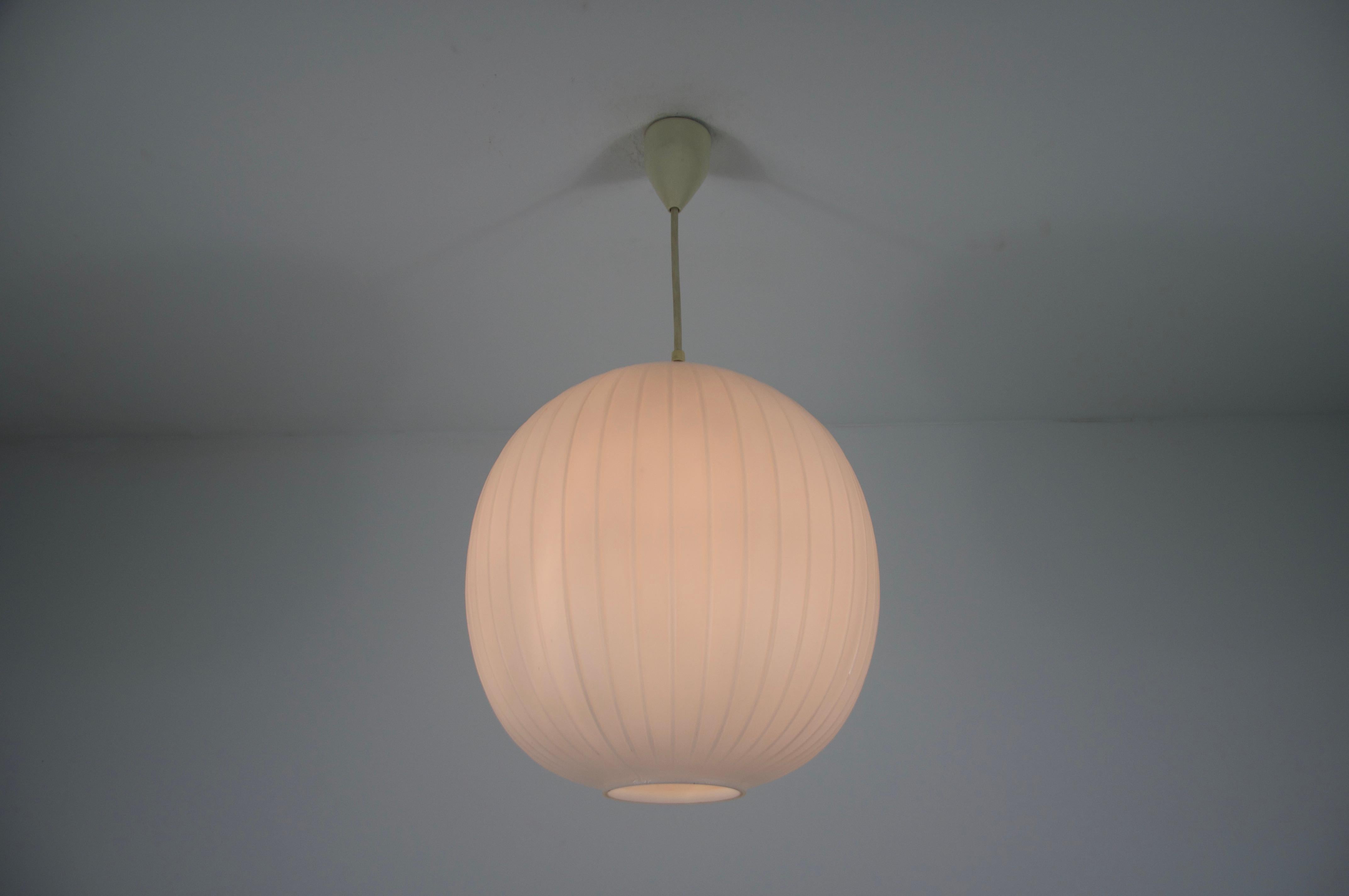 Questa elegante lampada a sospensione è stata disegnata da Aloys Gangkofner per Peill & Putzler negli anni Cinquanta. Il pezzo presenta un paralume sferico realizzato in vetro opalino con una sottile struttura a coste verticali, che crea un