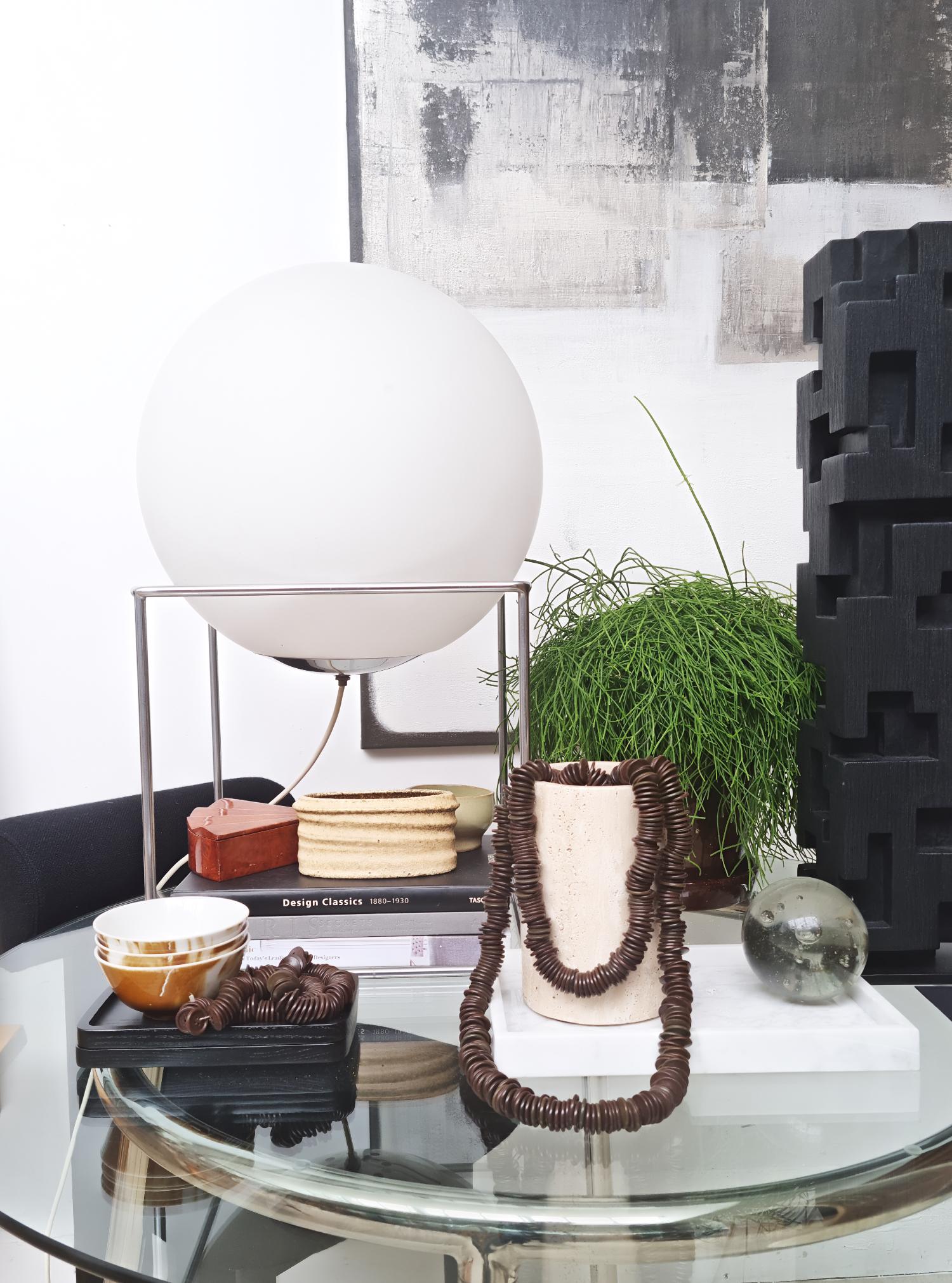 A square metal frame adorned with a single opal glass large sphere. Decorative and emblematic of the 1970s at its finest, this lamp captures the essence of the era. Its sleek design serves as a timeless representation, adding a modern and stylish
