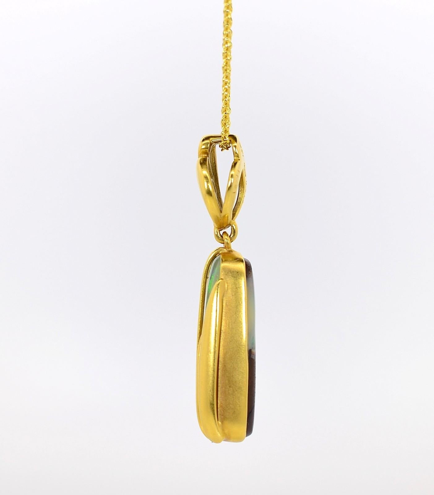 Artistically hand crafted in 18KT yellow gold this one-of--a-kind pendant showcases a beautiful lozenge shape 11.21 carat Boulder Opal.  The semi-translucent bezel set Opal radiates colorful patches of pastel blues and greens.  Dangling from a