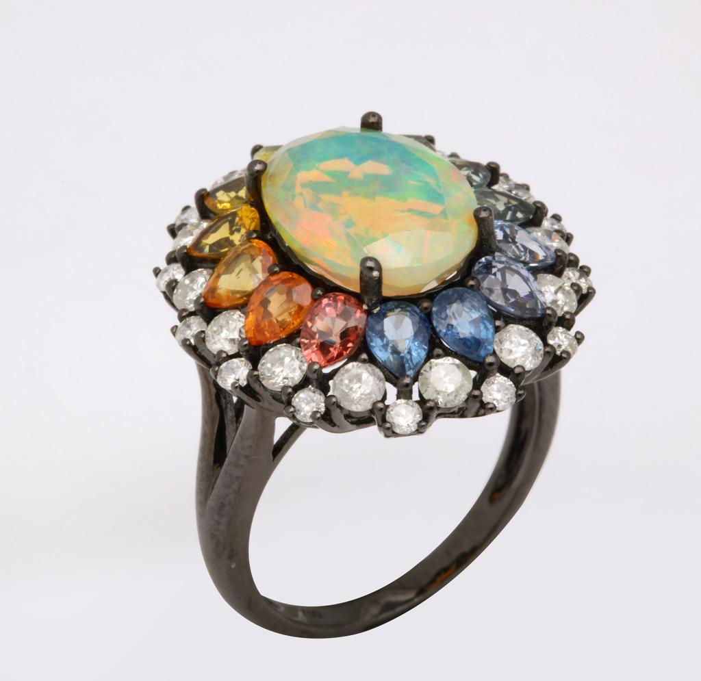 Bursting with color, this exceptional cocktail ring features a cabochon opal framed in multi color sapphires and diamonds.  The mounting is in 18kt blackened gold, which adds fantastic contrast to the multitude of colors.
Opal: app 2 1/2
