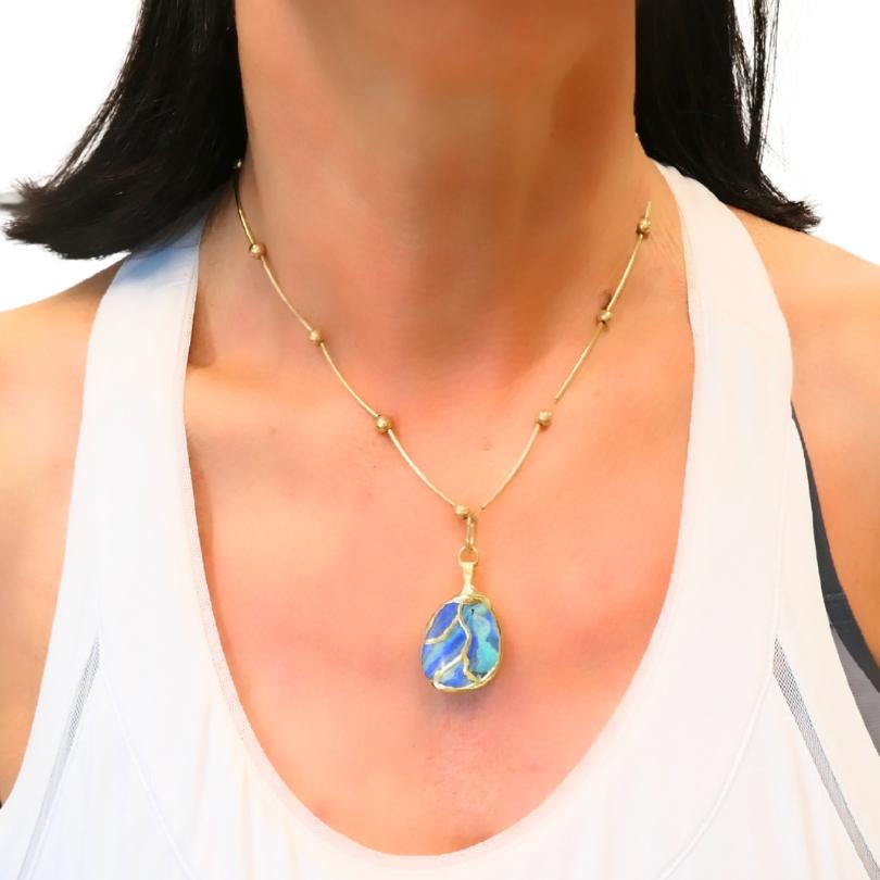 Un collar de ópalo, con una cadena de oro de 14 quilates acentuada por pequeñas cuentas de oro. La pieza central es un colgante de ópalo con singulares remolinos de color, engastado en un delicado marco de oro. El ópalo presenta una mezcla de tonos