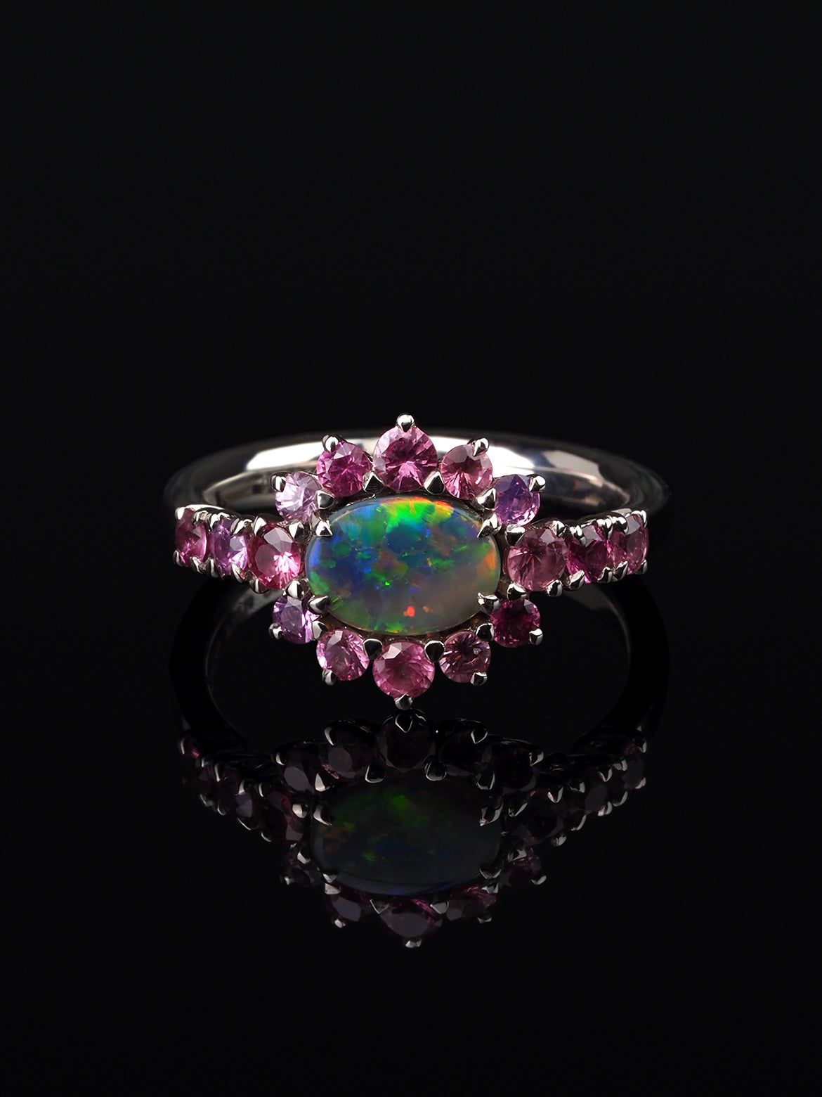 This contemporary custom made engagement/promise ring features a unique interplay of naturally beautiful gemstones. An Australian Opal is securely prong set sideways in the center, exhibiting an incredible play-of-color rainbow. This hand-selected