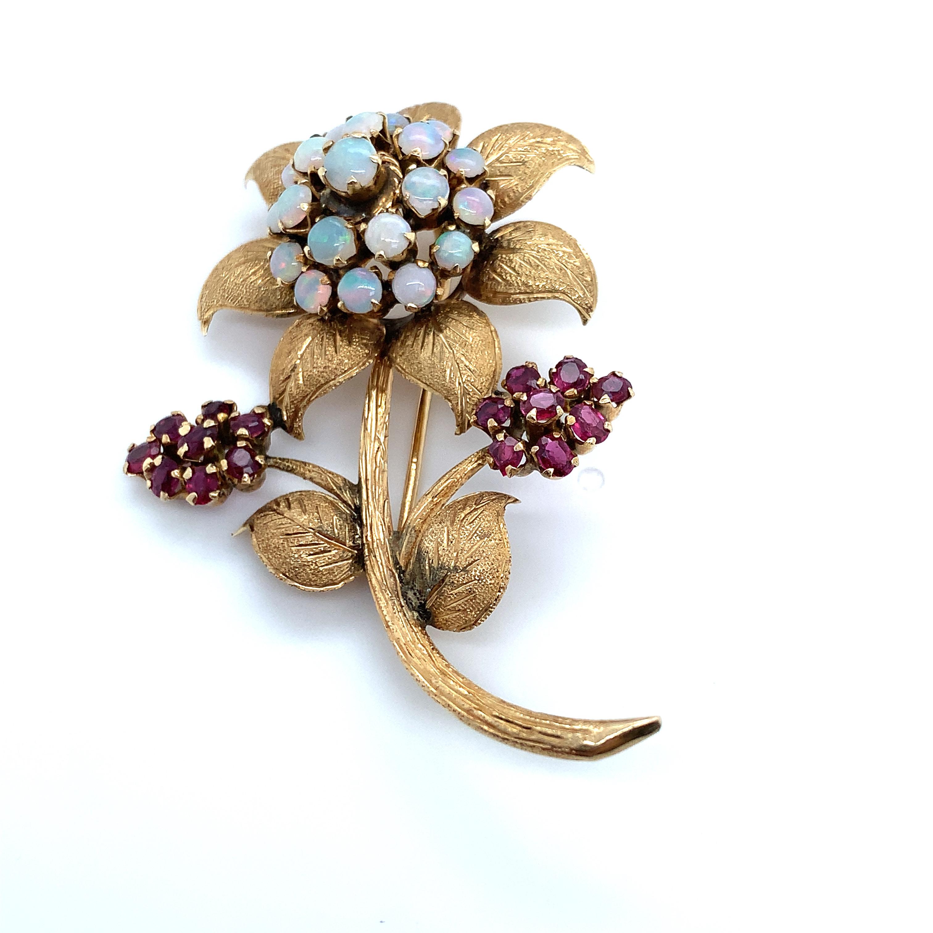 Elevate your attire with this vintage Opal & Red Gemstone Flower Brooch in 10K Yellow Gold. This timeless piece showcases an intricate flower design, made more appealing by radiant opal and red gemstones. The deep tones of the red stones strikingly