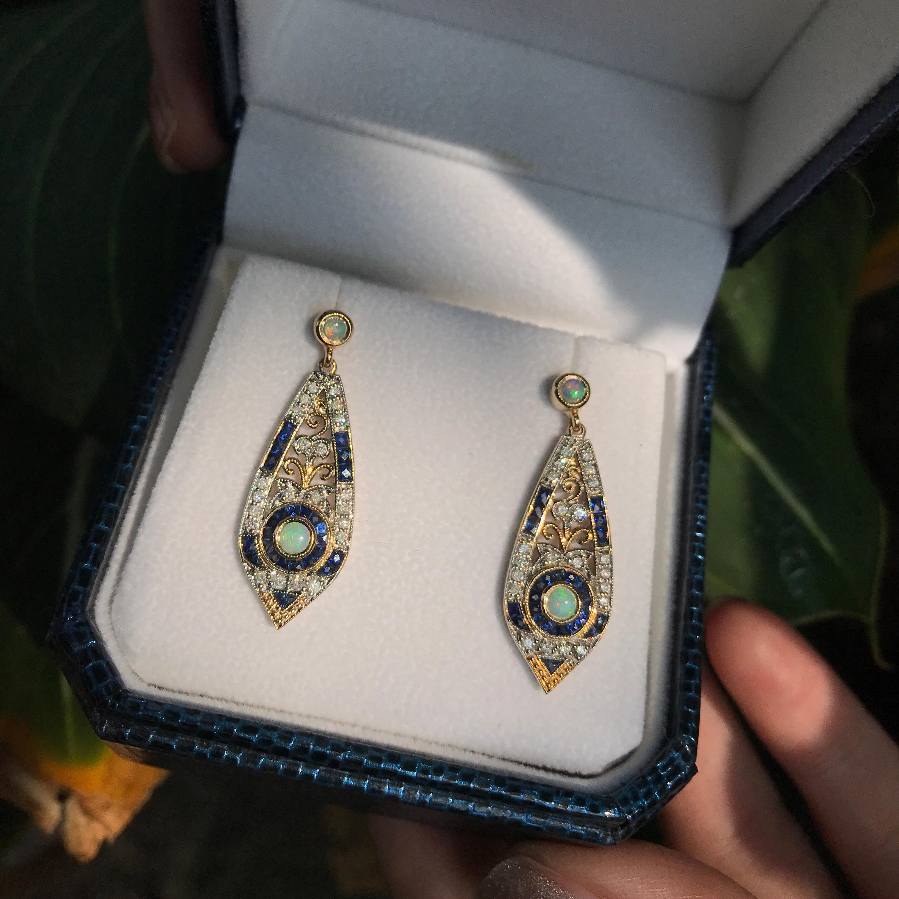 This is an exquisite pair of opal drop earrings with Art Deco ear design. The earrings feature a geometric design which is set with opals for their centers, surrounded by French cut sapphire and lovely sparkling diamonds, all set on 9k yellow gold.