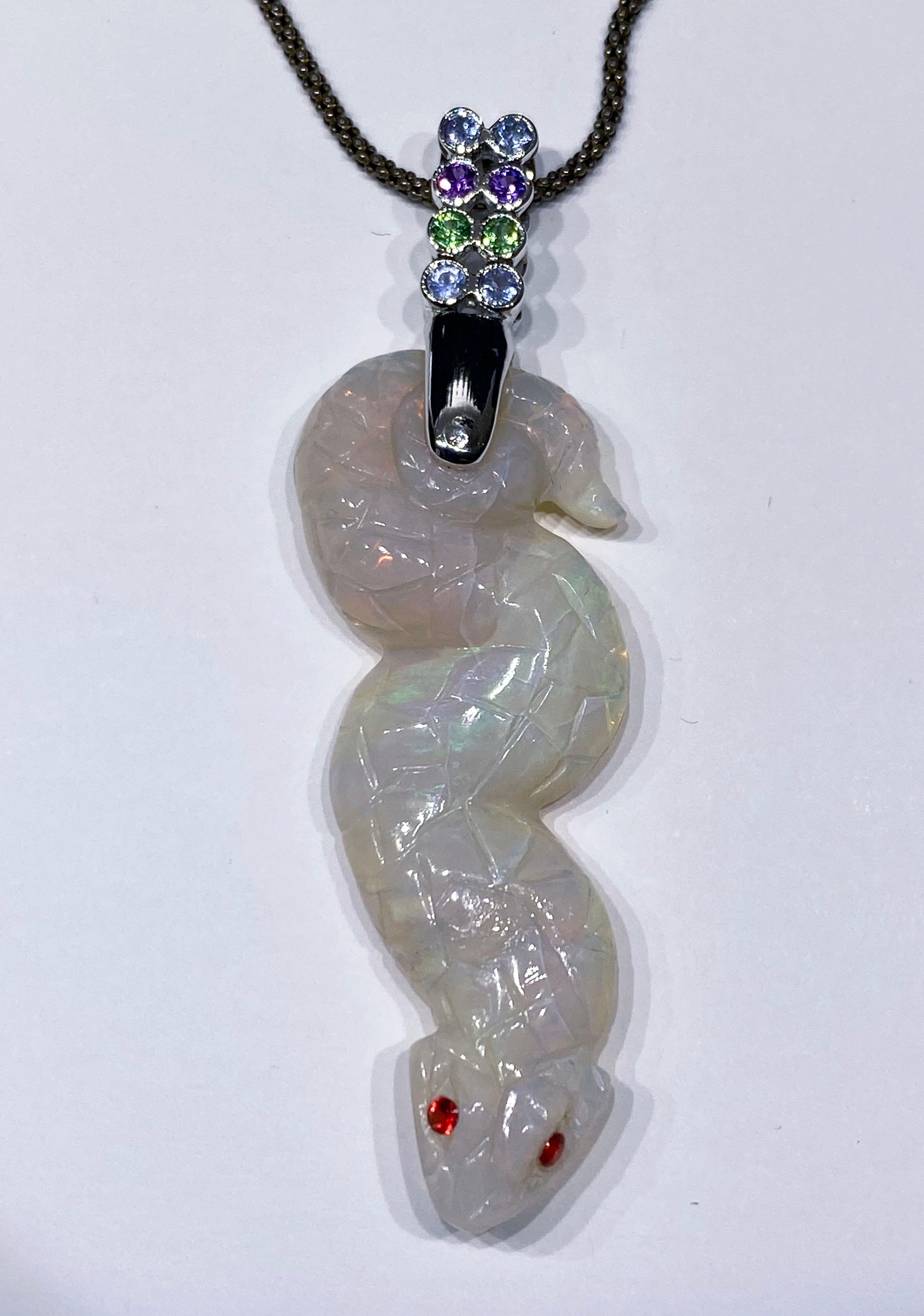 18kt White Gold Pendant with a Carved Opal Snake of 17 Carats Adorned with 8 Sapphire Rounds of 0.34 Carats in Blue Purple and Green. Hanging from a Blackened Silver Chain of 17