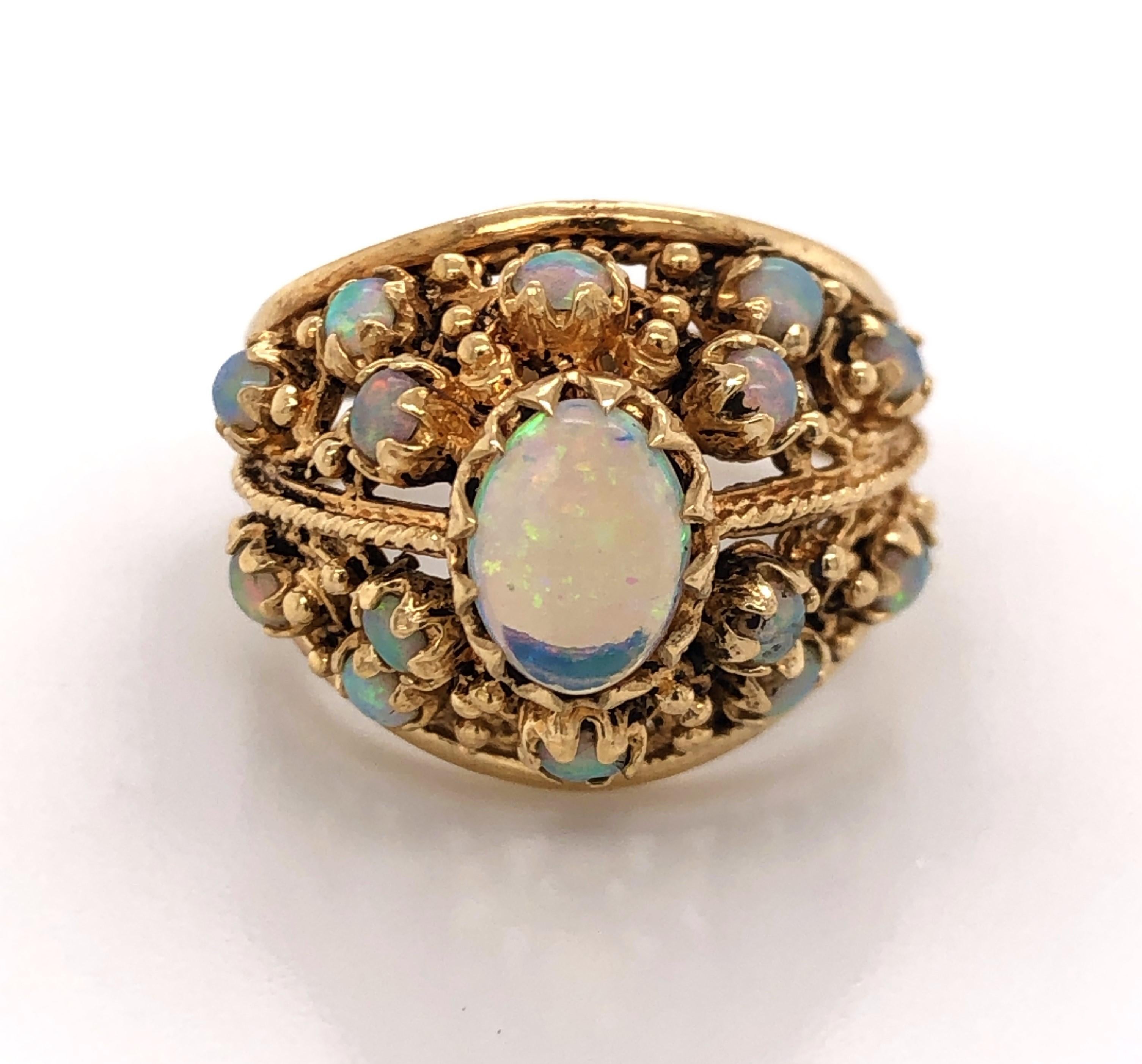 An effervescent pastel rainbow is displayed by this spectacular opal dome ring in fourteen karat (14k) yellow gold. Circa 1960's, the center stone is one 1/2 carat. Surrounding are fourteen opal accent stones, all individually prong set in fancy