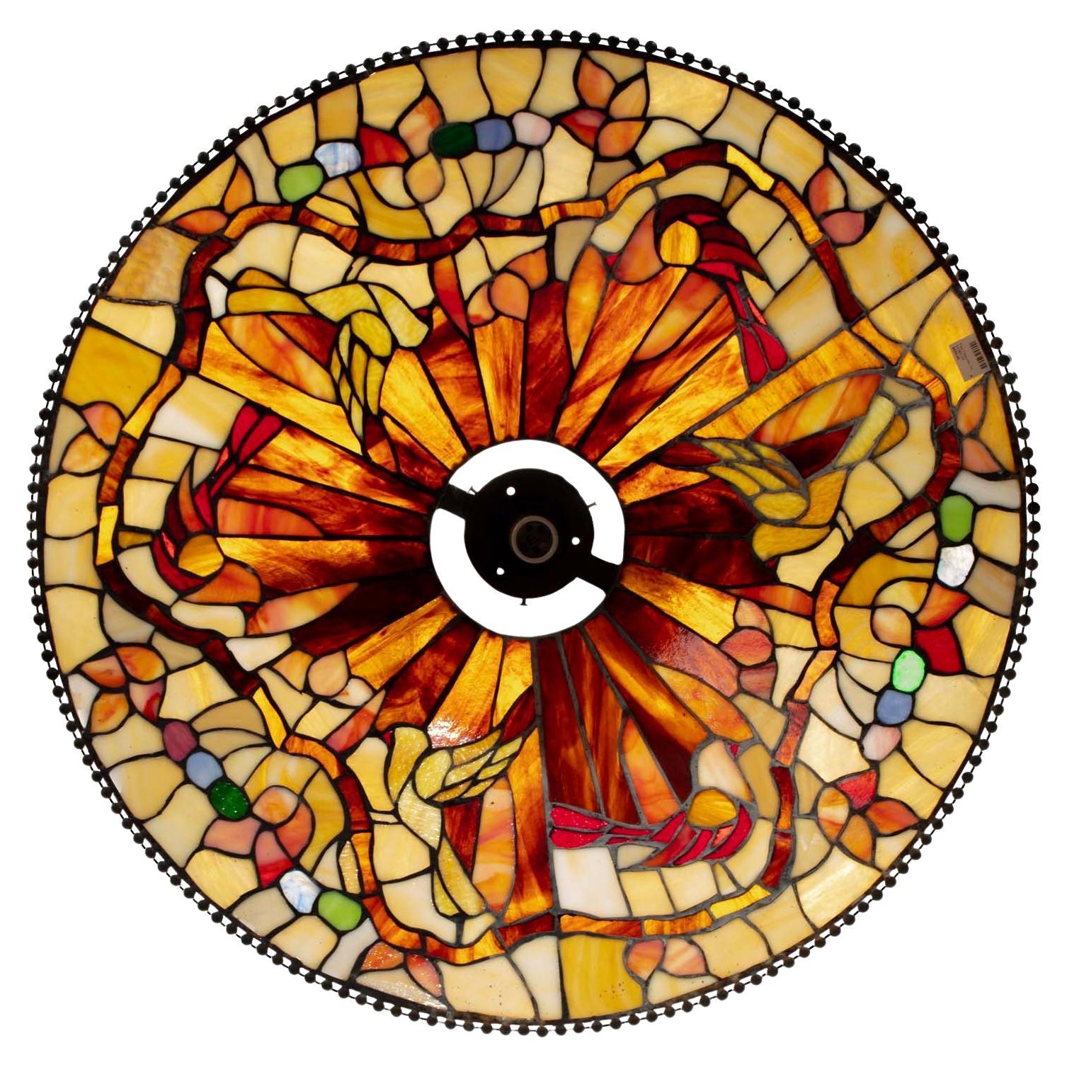 Realizzata nel periodo dell'Art Nouvea e nello stile di Louis Comfort Tiffany, questa lampada a sospensione in vetro colorato con perline in bronzo e una sola lampadina è ricca di colori caldi e opalescenti, dai toni naturali, disegnati con un