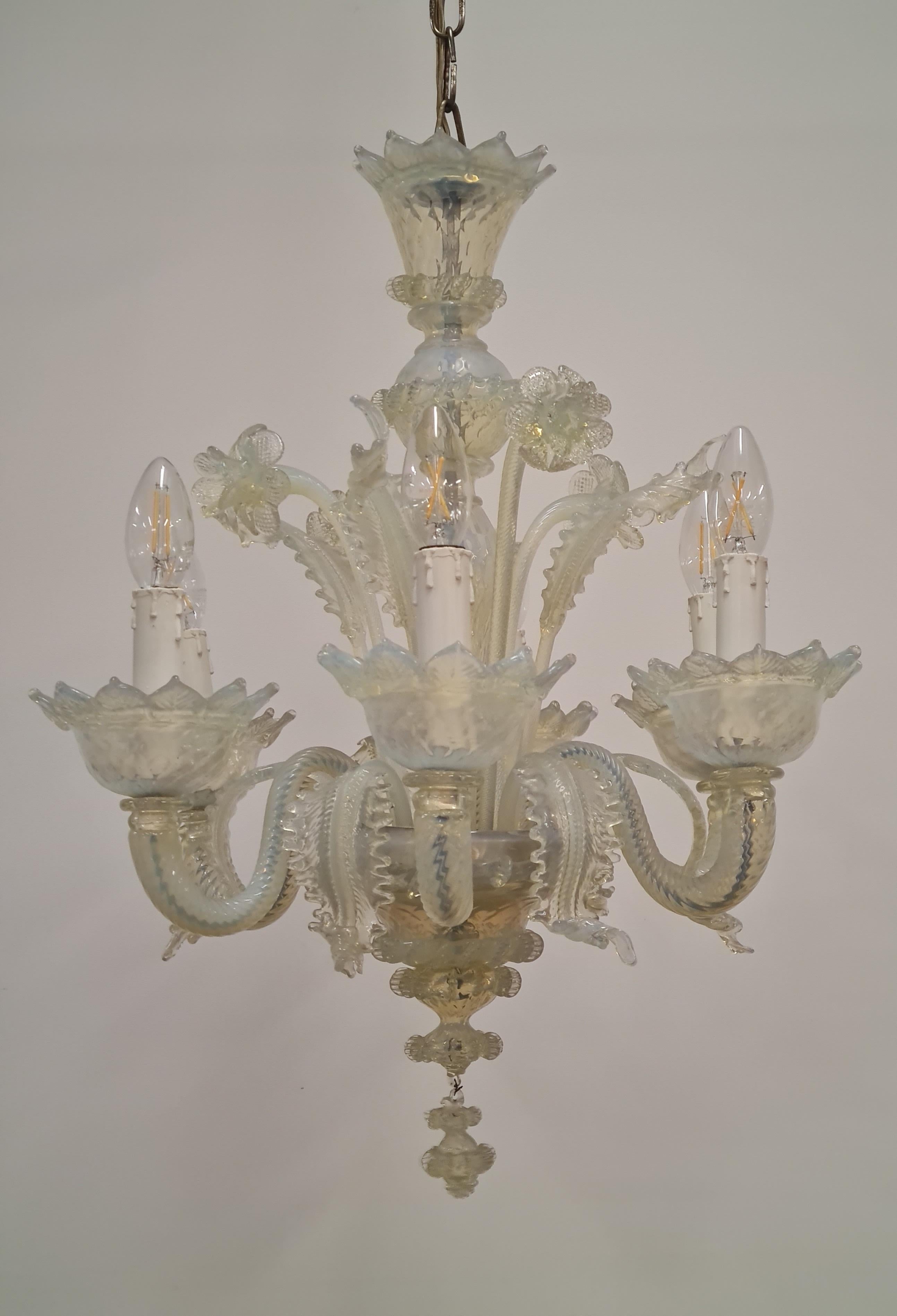 A beautiful hand made vintage Murano glass chandelier with six light arms and floral decorations. The lamps is made of art glass with an opalescent blue shade against the transparent milk white base with brass details and canope. A beautiful piece