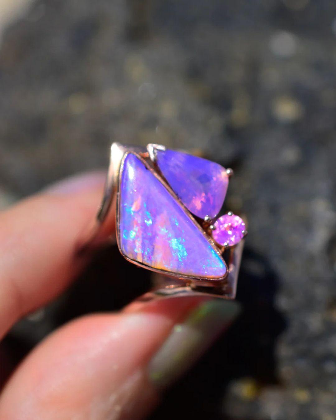 Opalescent Purple Sapphire and Purple  Australian Opal Symbiosis Ring in solid 14k Rose Gold. 23mm in length and 16mm wide.

This mouthwatering pairing of purple Australian 3D wood replacement opal with blue fire, is paired with purple and pink
