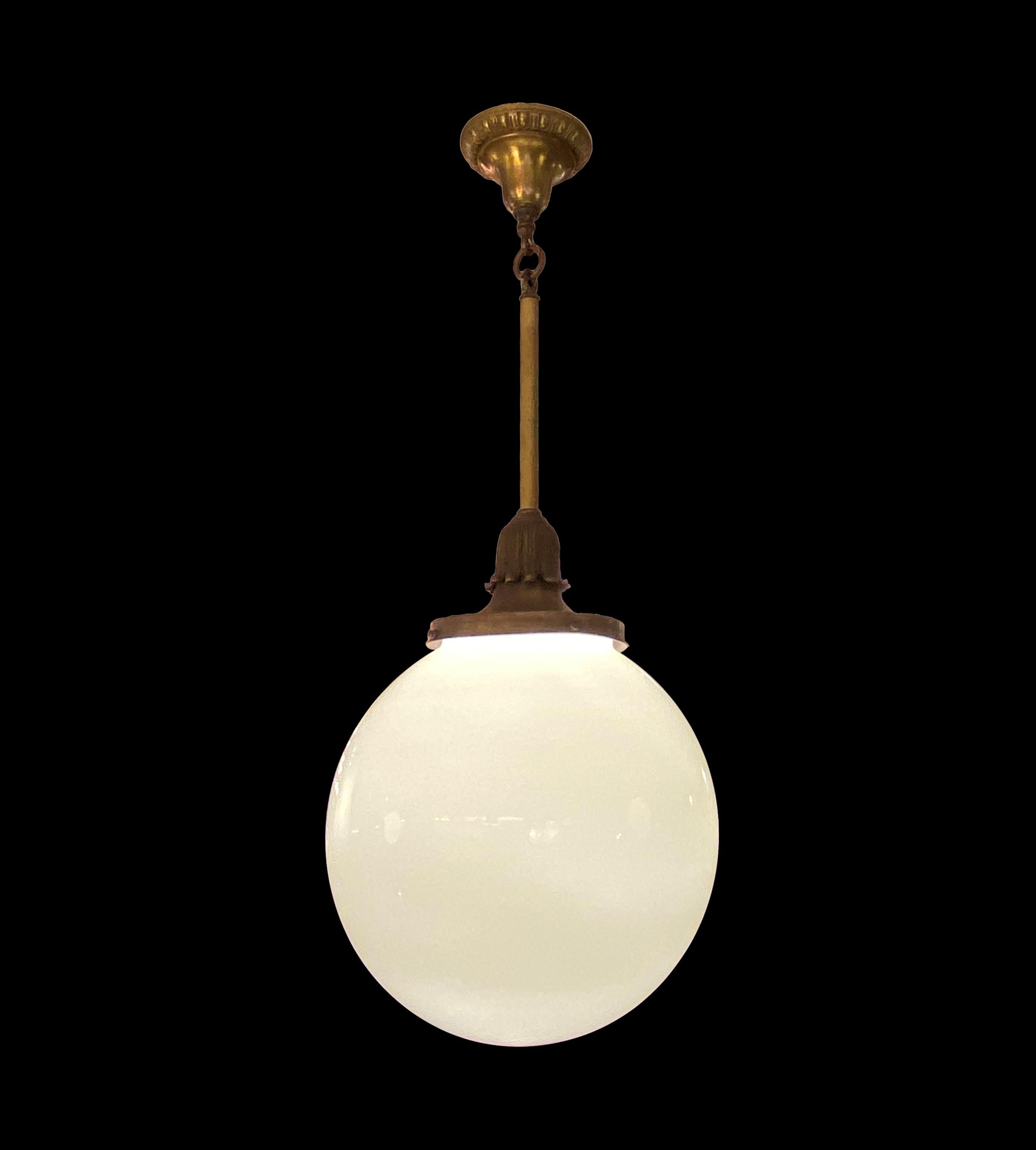 This pendant light is a captivating antique treasure. Its opaline ball globe, complemented by ornate brass and bronze accents, exudes elegance, adding a touch of timeless charm to any space. Cleaned and restored. This light requires one medium base