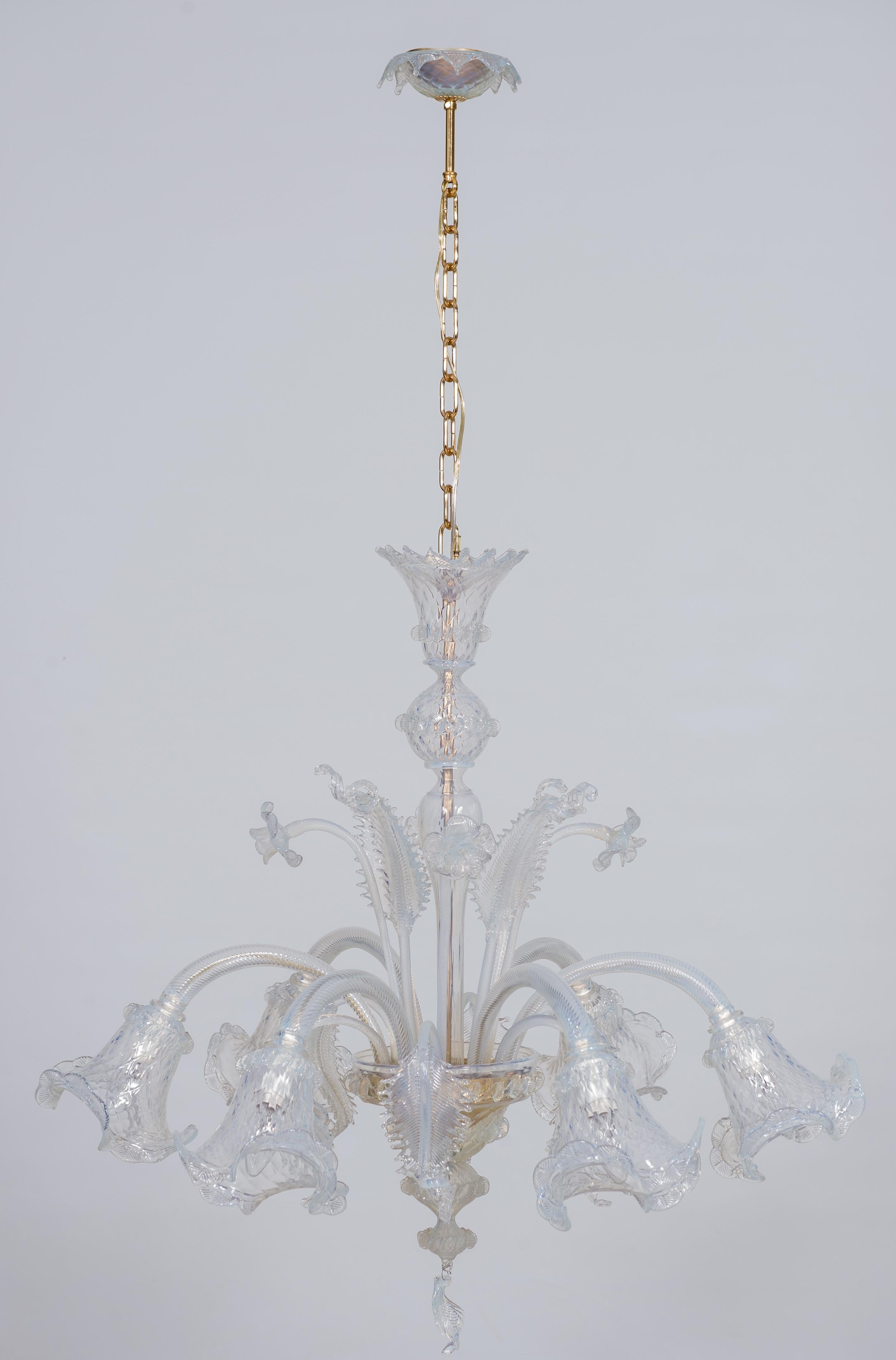 Opaline Chandelier in blown Murano Glass gold frame with flowers 1990s Italy.
The central stem is made of opaline glass, and goes from the ceiling down to the base of the chandelier, from which six transparent arms spread out, gently bend downwards,