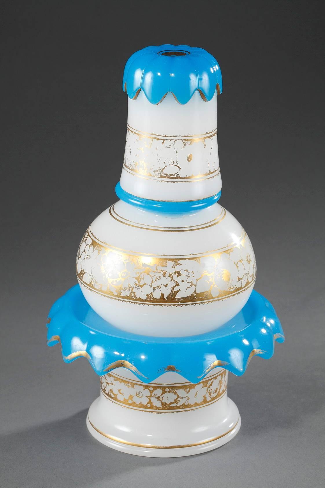 19th century white and blue opaline set composed of a water glass, a bottle-shaped flask, and a spittoon that forms the base. The three pieces are decorated with gilded friezes of flowers and stripes. Saint-Louis Glassworks. 

circa