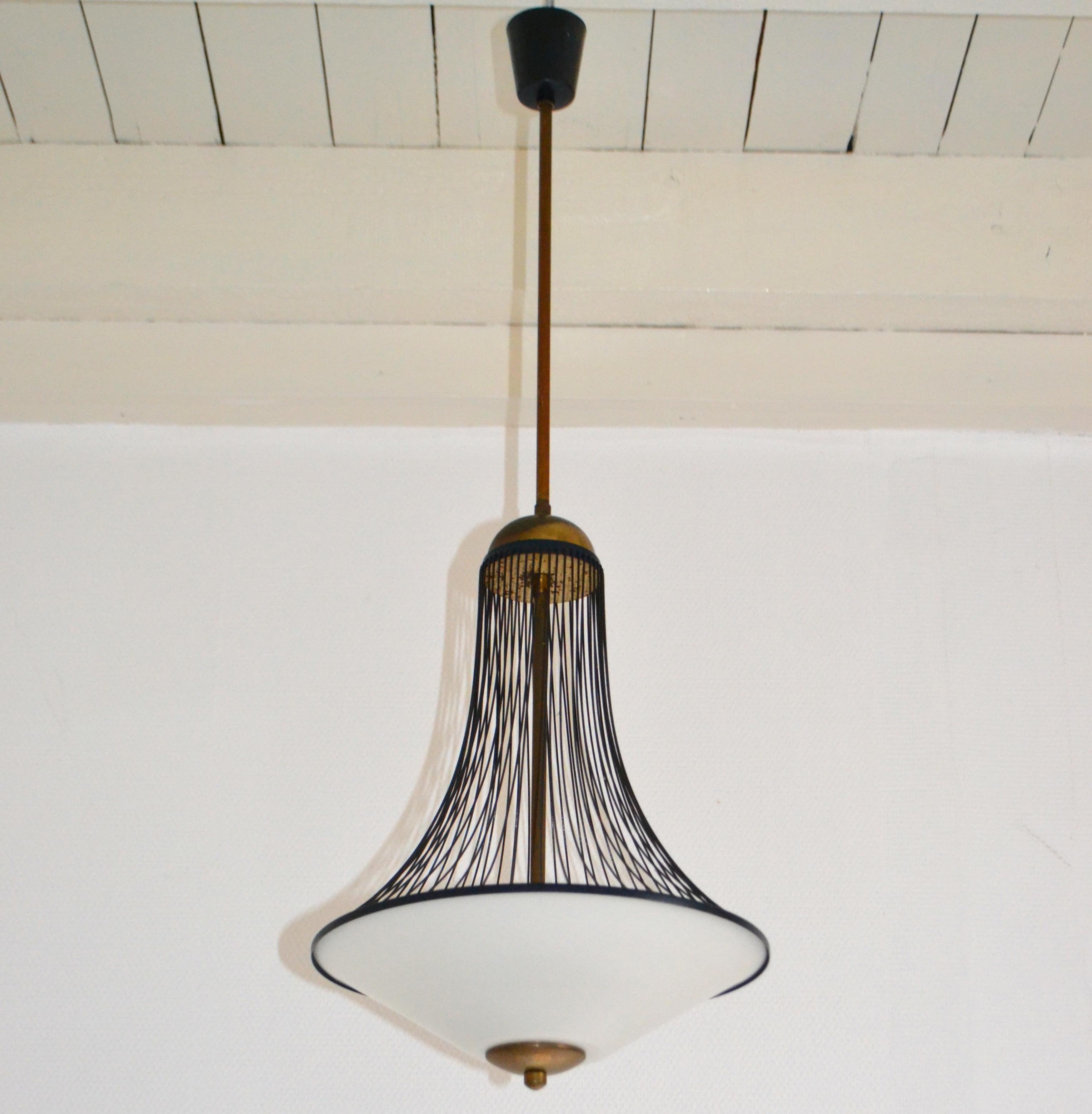 Italian 1960's pendant or lantern has a milk glass shade connected to a curvaceous open wire metal frame and brass connections.
This pendant lamp suggesting a lantern is very functional for general light and most suitable for a hallway center