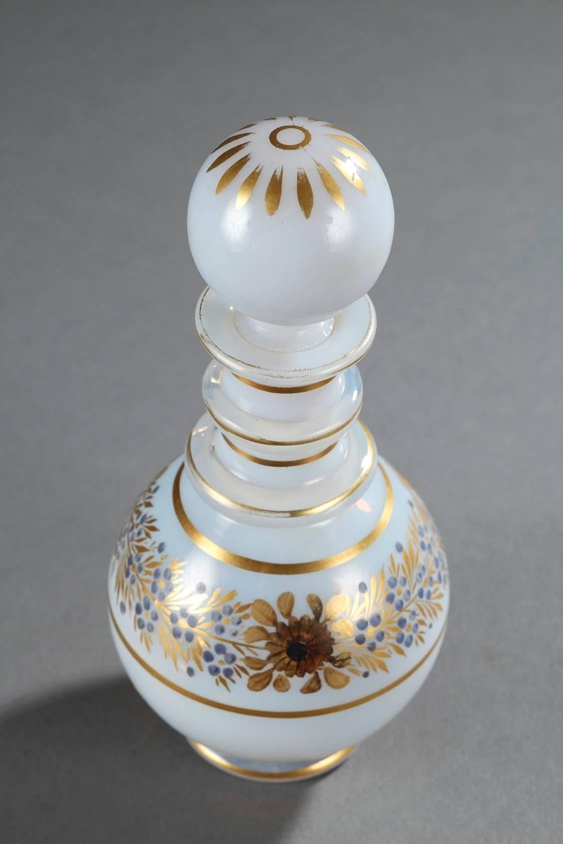 Small perfume bottle in white opaline with a ball-shaped stopper. Golden stripes, gold, and a dark blue wreath of roses, anemones, and forget-me-nots decorate the rim of the paunch. The top of the stopper is highlighted with petals. The decoration