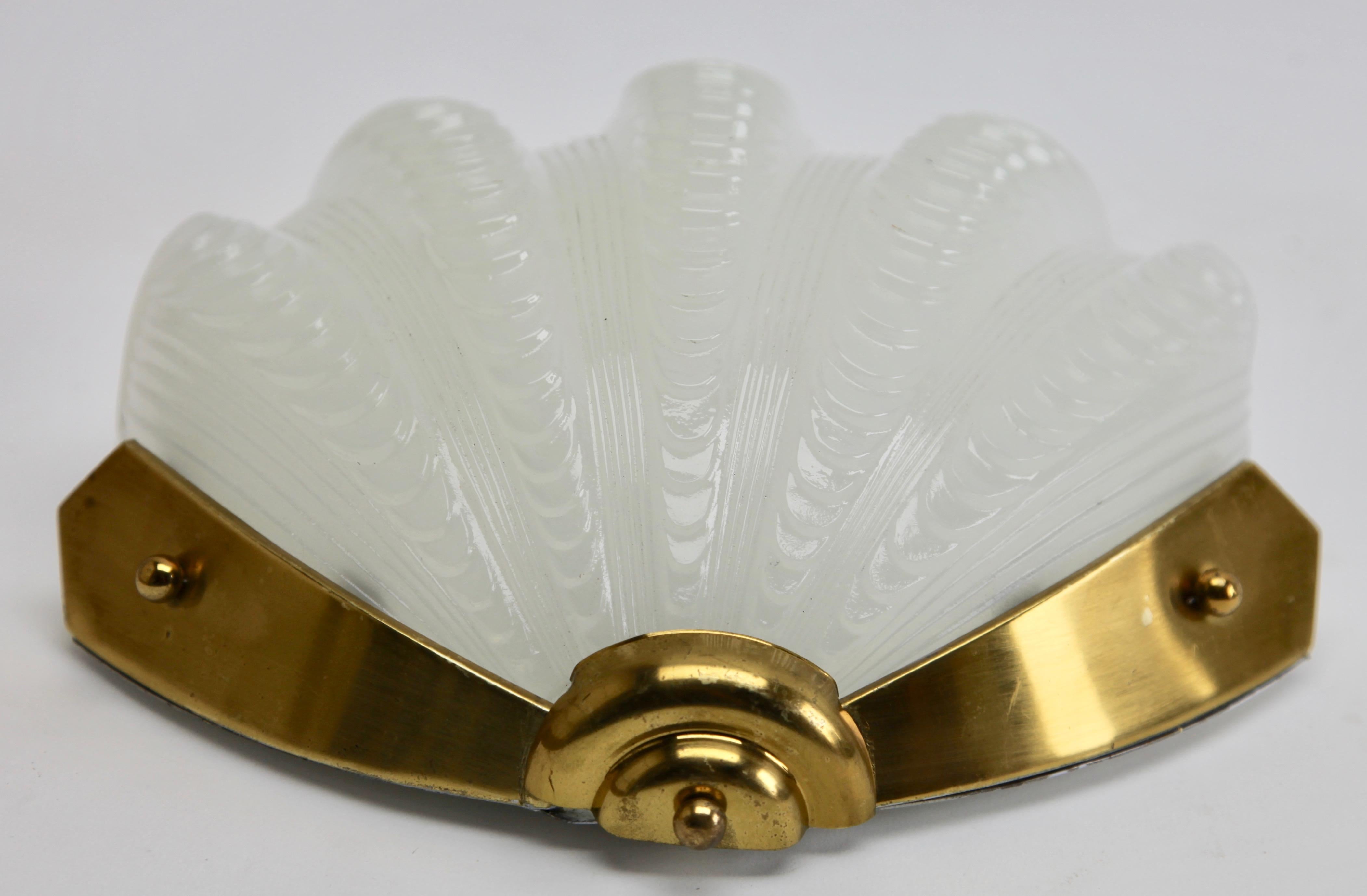 Period wall sconce with a shade modelled as a clamshell. 
Heavy opalescent white glass shade made of pressed glass, securely held in a wall-mount bracket. Good condition with no damage to the glass or metal parts.

Gives soft subdued light for a