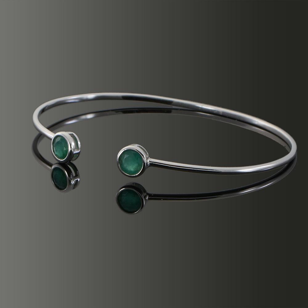 A sleek and refined open bangle in 18KT white gold, accented by two vibrant bezel-set round emeralds totaling 0.70 carats. The clean lines and open design make it perfect for stacking or wearing alone as a subtle statement of sophistication. A