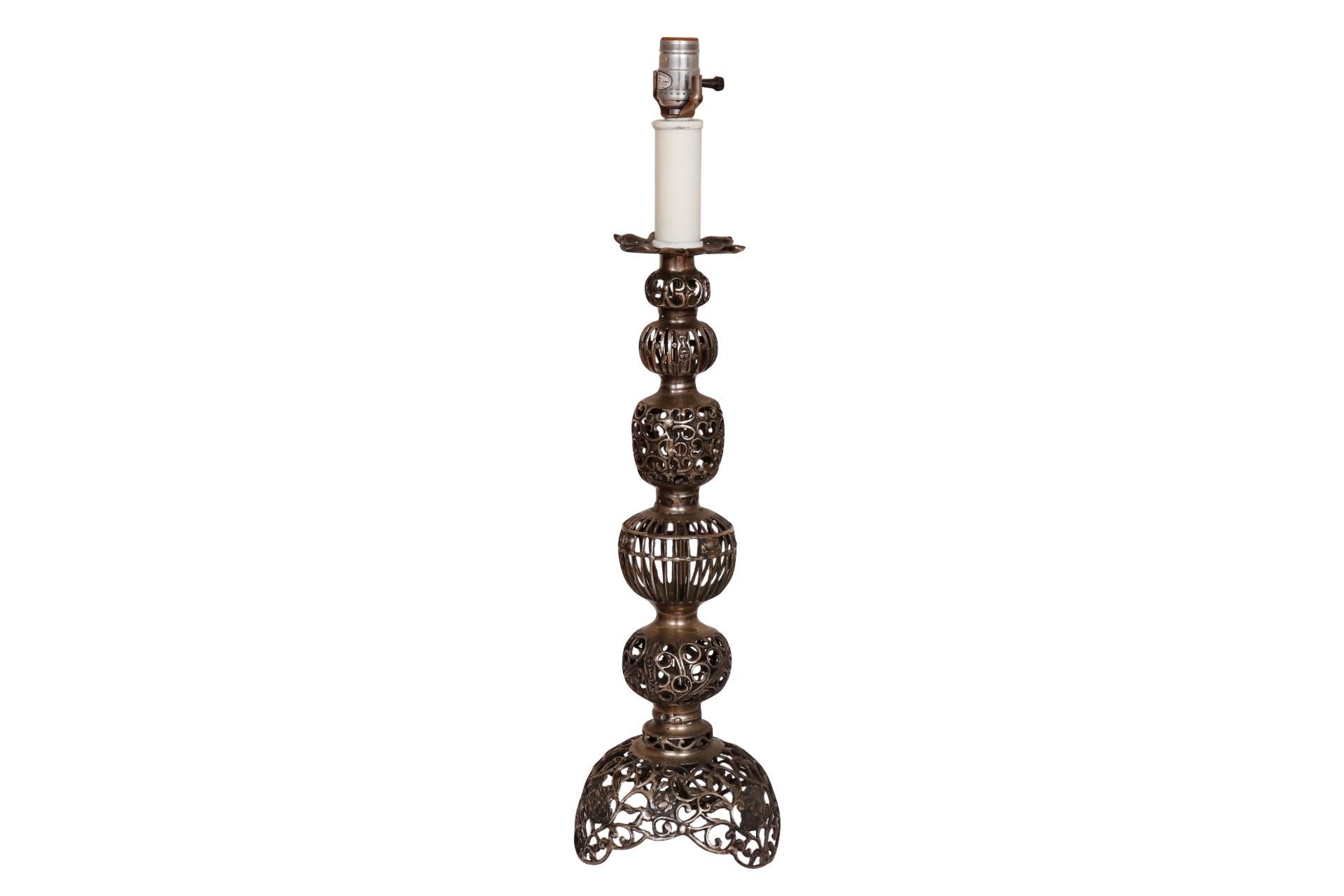 An open metal baluster table lamp by Tyndale. Sections are cast with small s-scrolls, cages and vine like metalwork accented with pressed roses. The base is shaped with three feet.