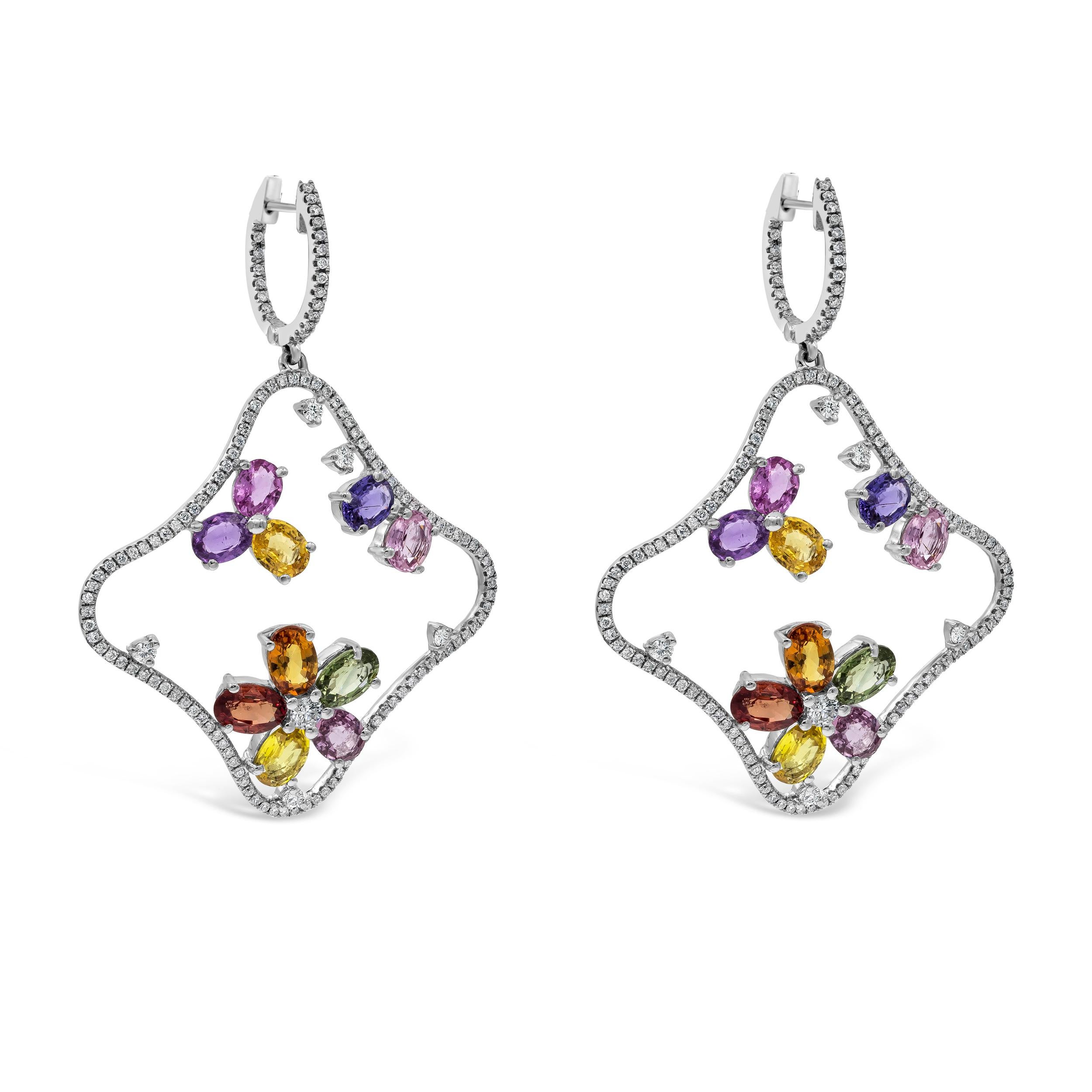 A wonderful pair of dangle earrings, featuring oval cut multi-color sapphires weighing 9.67 carats total, set with a floral motif in an open-work design. Accented by melee round diamonds weighing 1.18 carats total. Finely made with 18K white