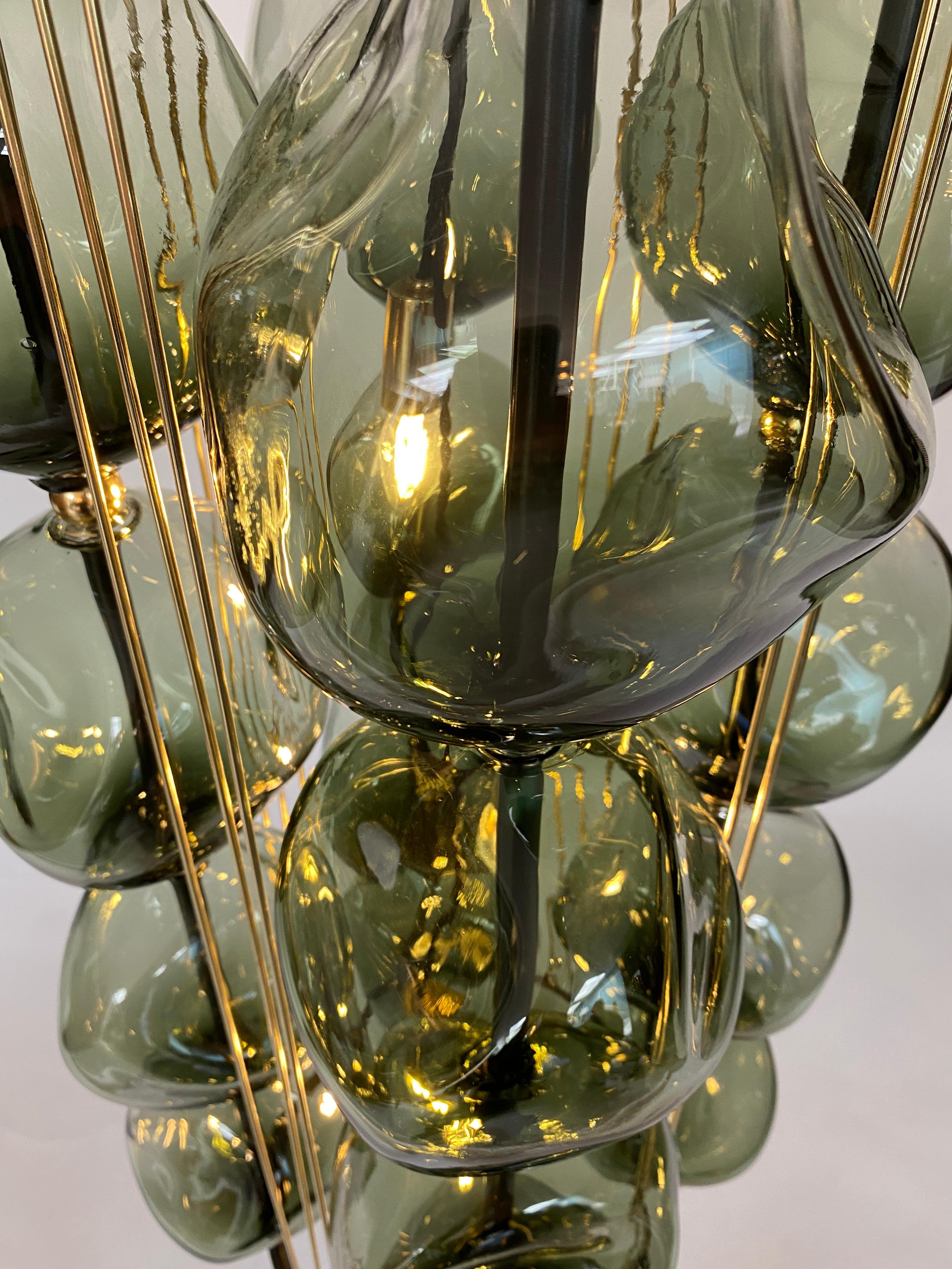 16 orbs hand blown in hunter green Glass glass are assembled on a steel frame with a gun metal patina. The chandelier has brass accents. The light uses 3 candelabra based sockets, Max wattage 60 each bulb.