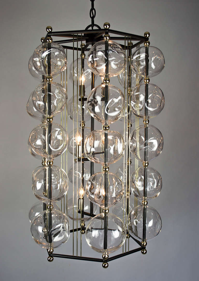 A fresh expression of the classic lantern created to accentuate the shimmering light which reflects in the many contours of the glass. The hand blown glass orbs with their asymmetrical shapes are assembled on a hexagonal gunmetal steel frame. The