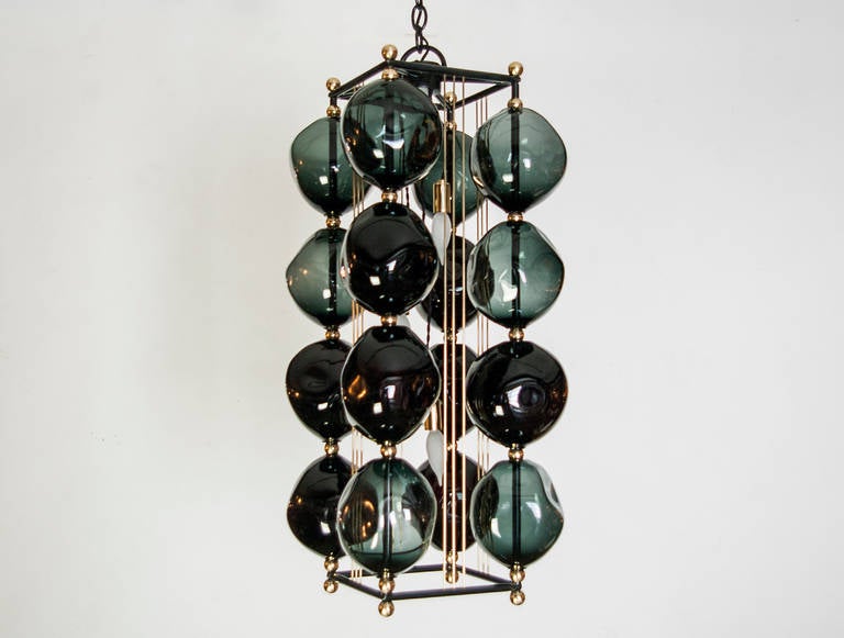 16 orbs hand blown in black glass are assembled on a steel frame with a gun metal patina. The chandelier has brass accents. The light uses three candelabra based sockets, Max wattage 60 each bulb.