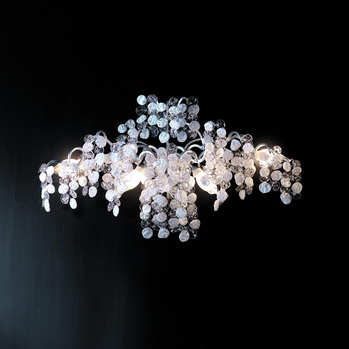 The resplendent allure characterizing this wall lamp is particularly evident in its splendid ensemble of hand-tied white and transparent glass petals creating a cascade that stunningly reflects the light cast by the four ES bulbs (G9 and max 33W