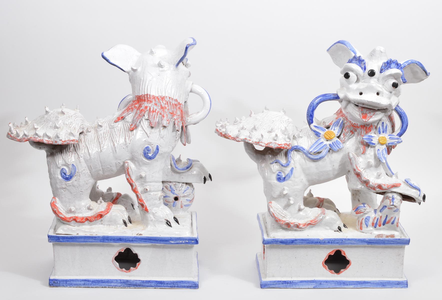 Standing 21 inches tall this pair of whimsical Majolica white glaze ground foo dogs on matching bases are sculpted in the manner of Ugo Zaccagnini; They are decorated in blue, coral red and yellow creating a light and uplifting impression.