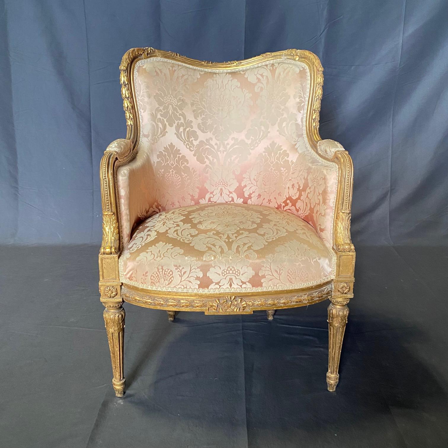 Exquise paire de bergères en bois sculpté et doré de style Louis XVI provenant d'un salon complet. Le design, avec ses lignes élégantes de style Louis XVI et sa décoration délicatement sculptée à la main, témoigne d'un grand souci du détail. La