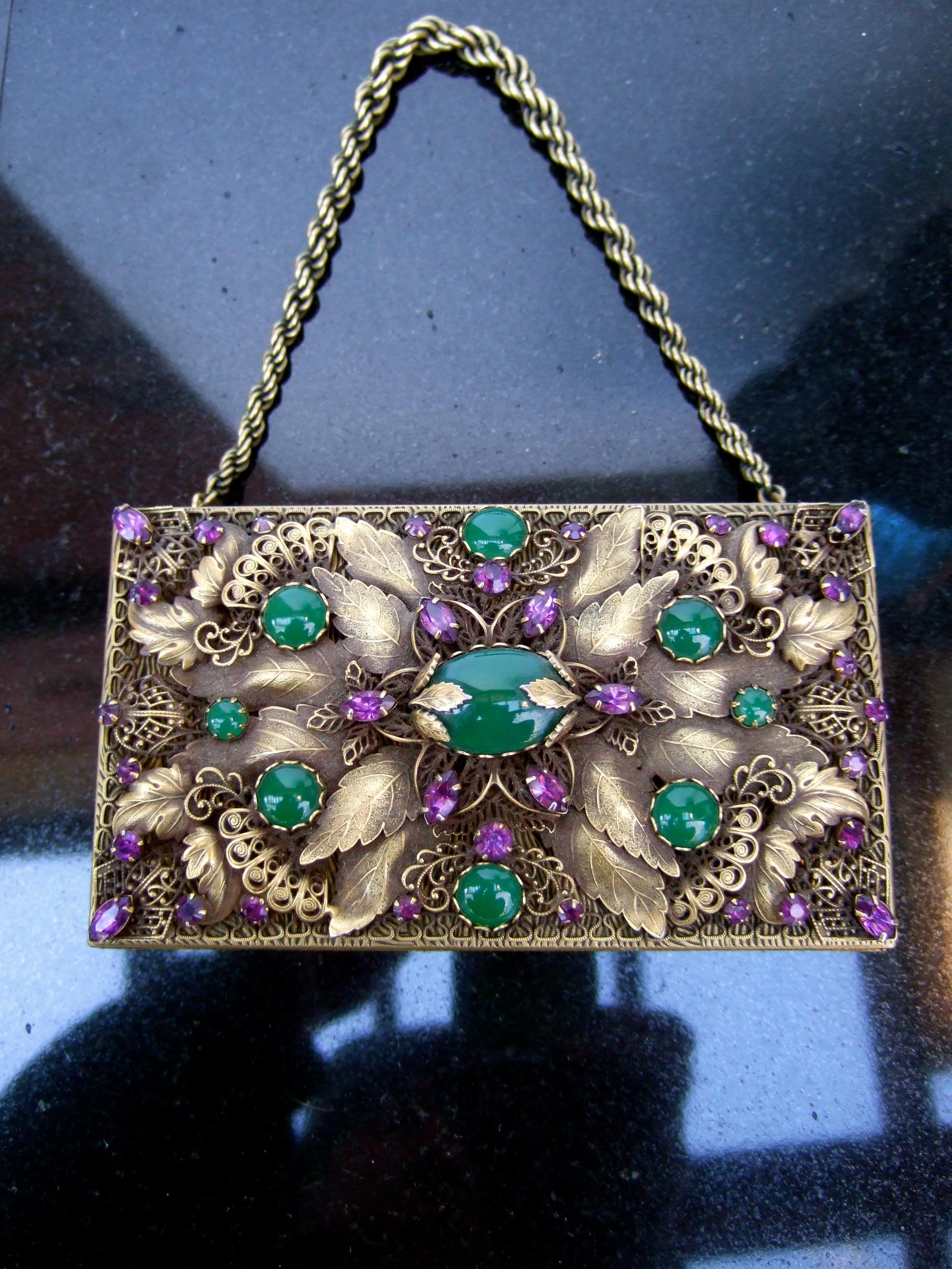 Opulent jeweled brass metal filigree evening bag - compact case designed by Evans c 1950s
The exquisite evening bag is encrusted with smooth green glass chalcedony color glass cabochons
Accented with clusters of amethyst color prong set crystals.