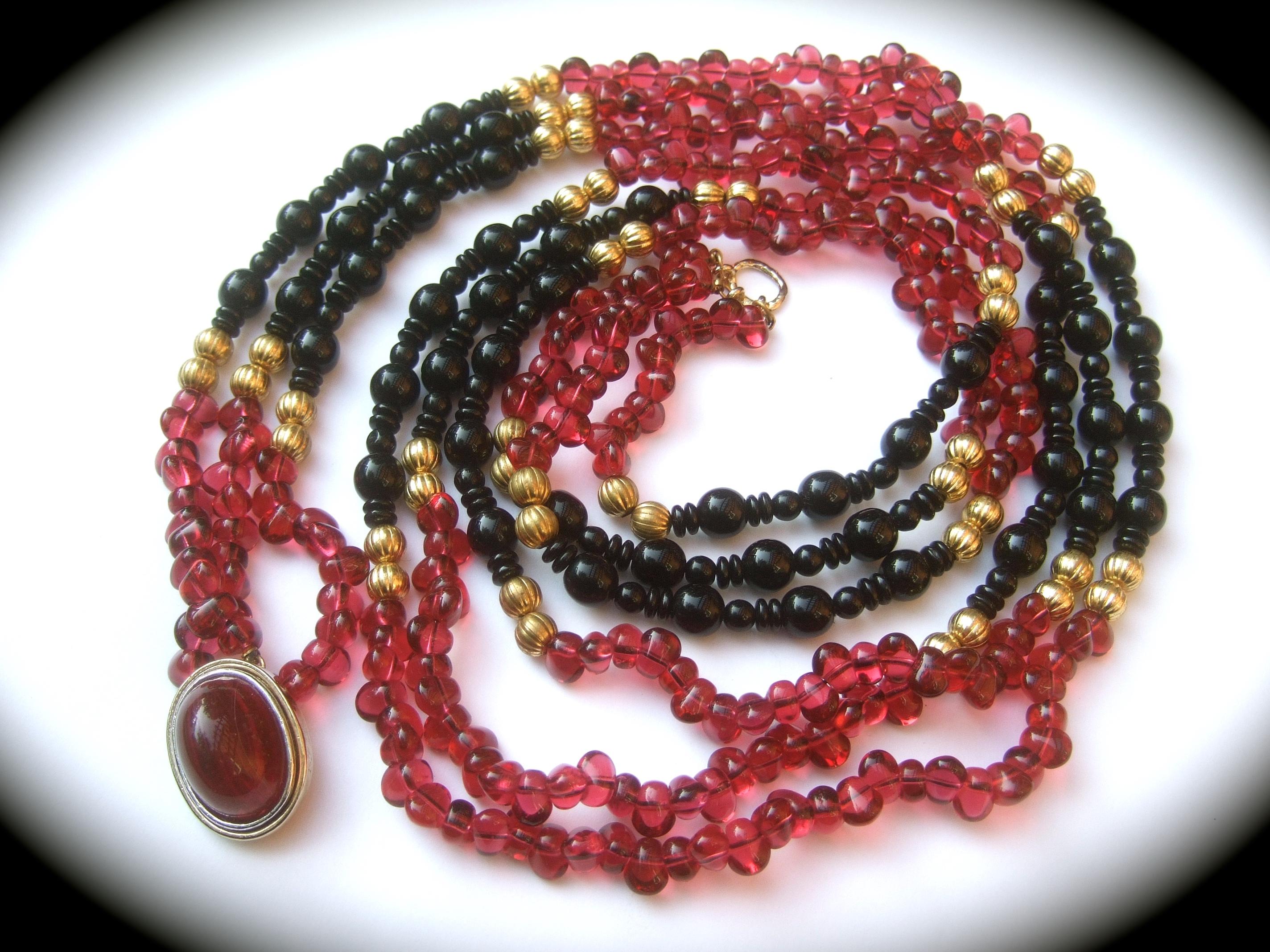 Opulent long glass beaded triple strand statement necklace c 1980s
The elegant opera length necklace is comprised of a collection deep berry color smooth oval irregular shaped translucent beads; juxtaposed with rows of jet black beads in various