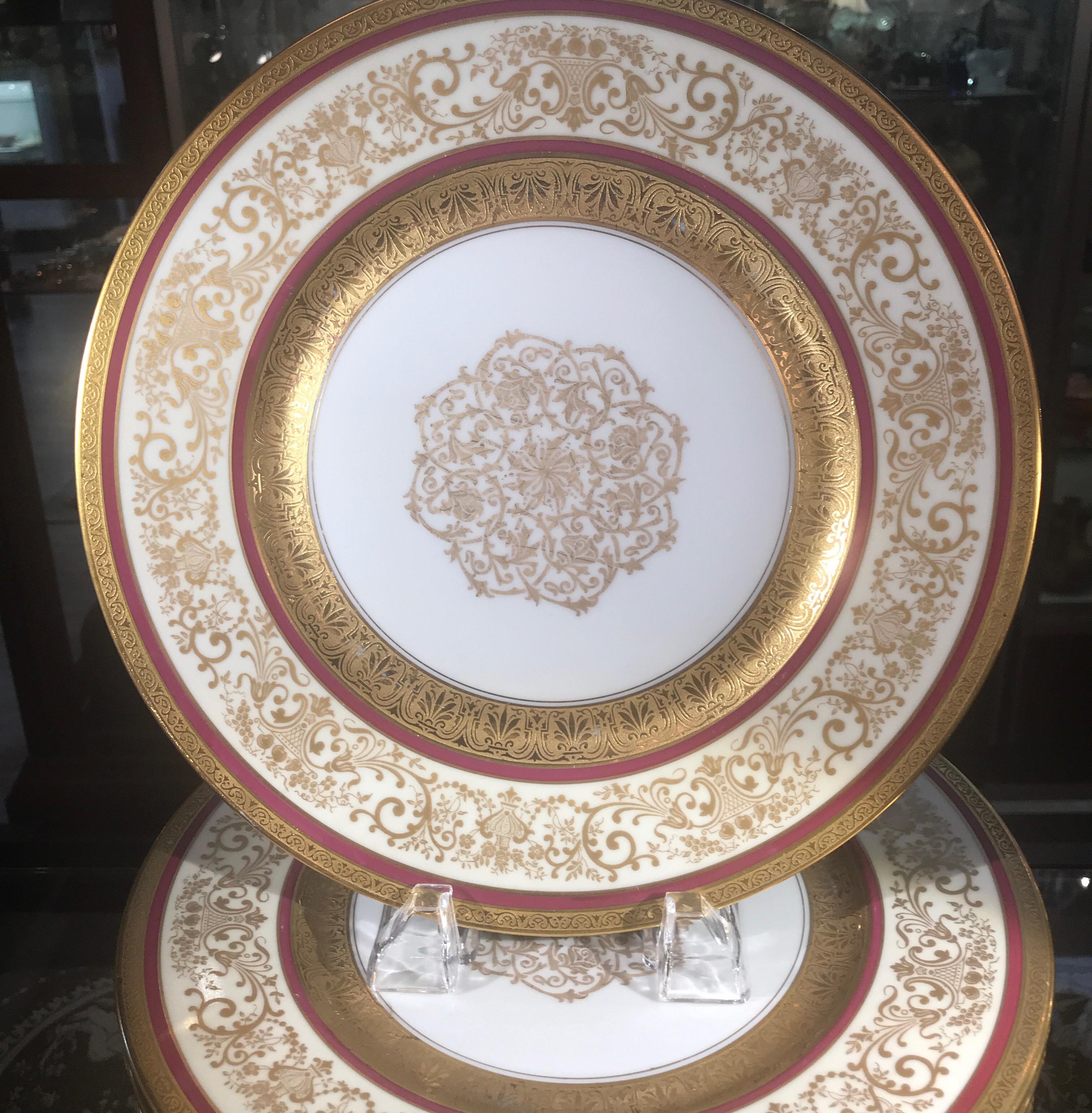 Elegant set of 12 elaborate gold banded service plates with berry trim. The gold encrusted borders with two thin red cranberry rings with filigree gold medallion centers. Excellent condition. Set a magnificent table or display in a cabinet.