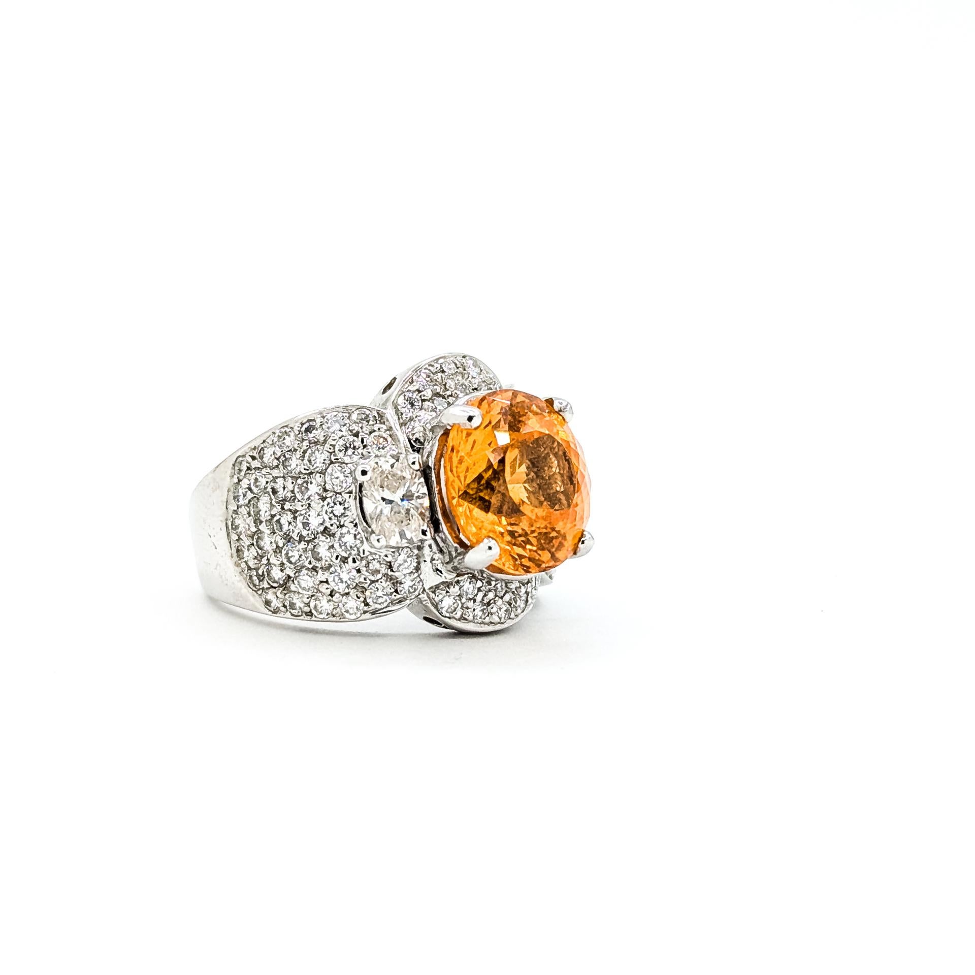Cette bague saisissante est réalisée en or blanc 18k et met en valeur de vibrants grenats spessarites orange sertis en pavé, pesant 3,5 carats. Le design large et audacieux est rehaussé par un ensemble éblouissant de diamants ronds et ovales presque