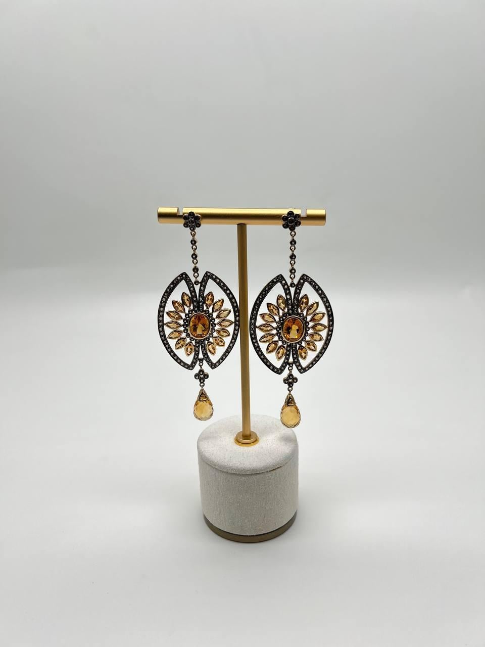 These dangle earrings feature intricate citrine stones set in a detailed design. The earrings showcase a central citrines surrounded by a sunburst pattern of smaller stones like diamonds and other citrines, all framed within a marquise-shaped