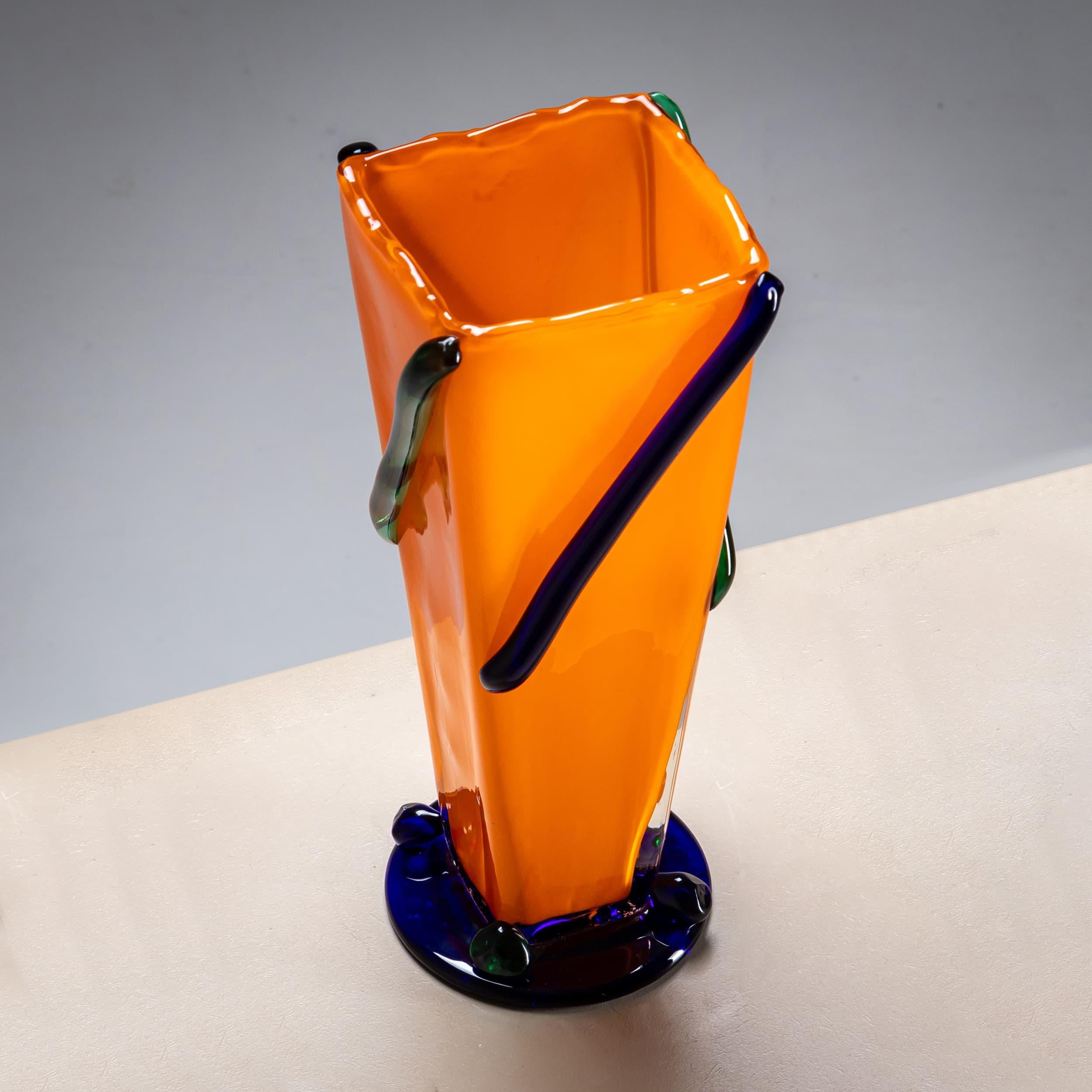 Large vase featuring a round base and a pyramidal body crafted from opaque orange glass. The surface is adorned with diagonal green glass stripes, and the top edge exhibits an irregular wavy design. Signed at the base: J. Guliajile.