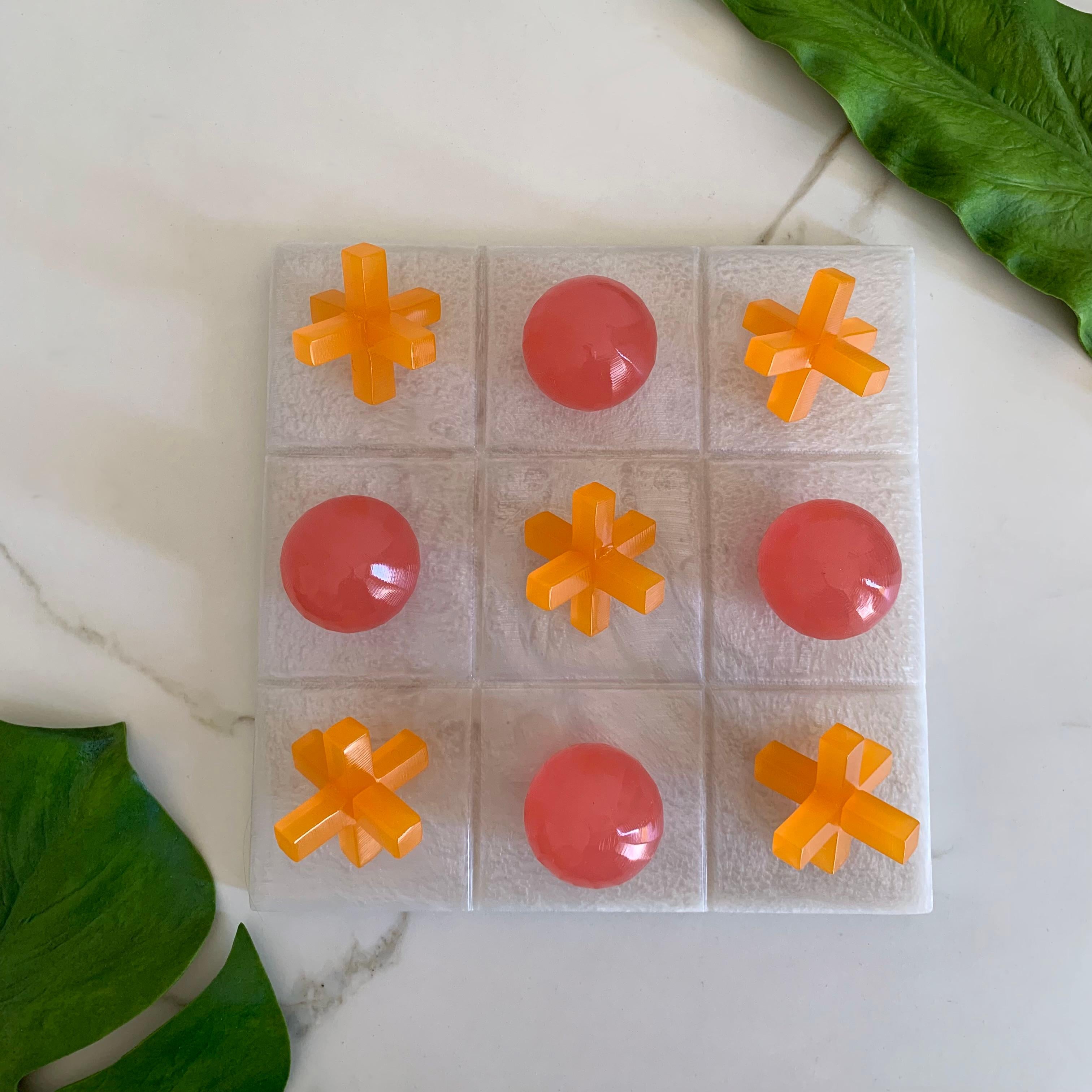 Unser Tic Tac Toe ist eine schöne, moderne und lustige Version des klassischen Spiels. Die dreidimensionalen Stücke sind aus rosa und orangefarbenem Harz handgefertigt, und das Brett ist aus weißem Perlenharz. Es wird das coolste Stück auf jedem