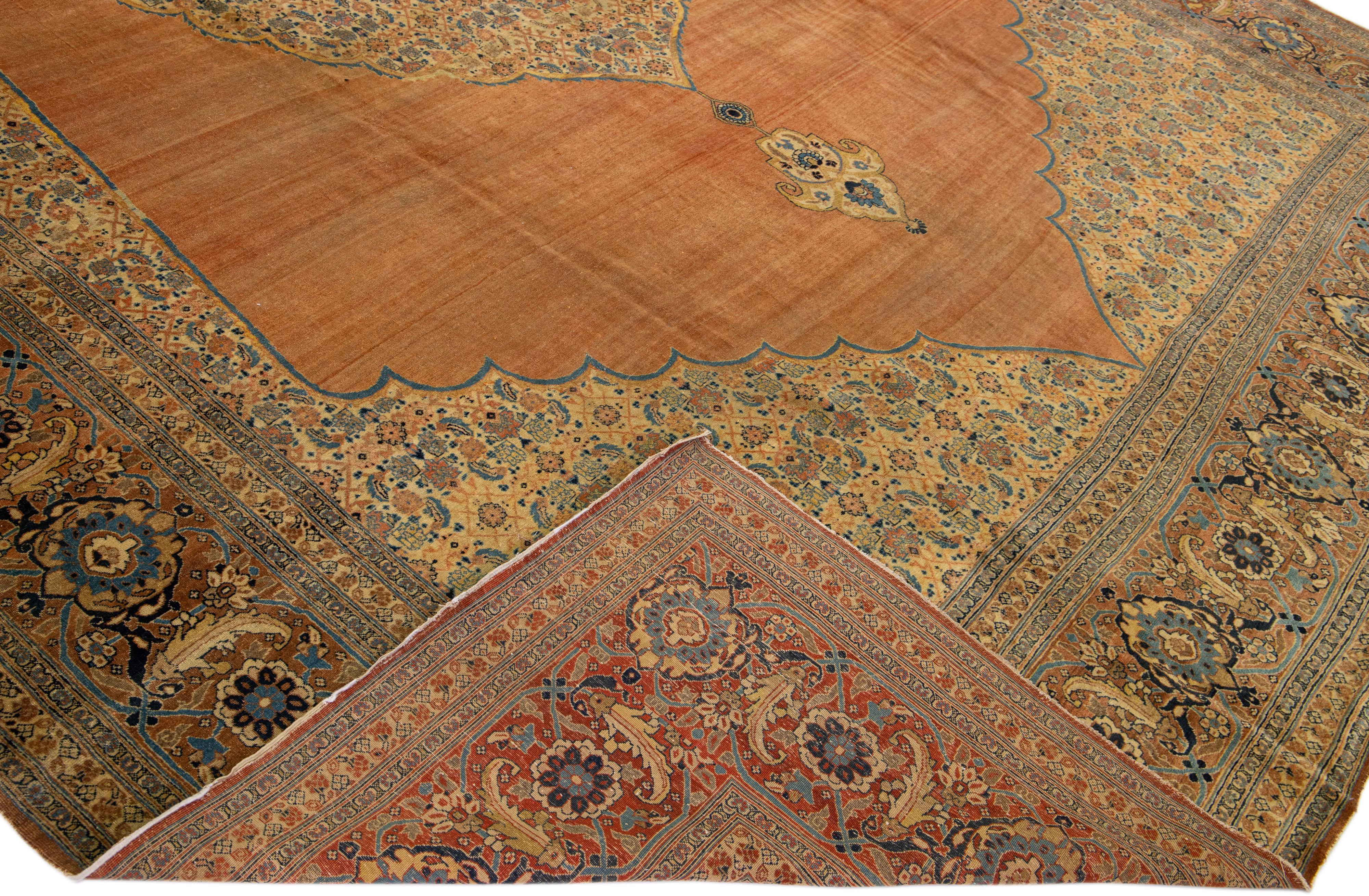 Beautiful Antique Tabriz hand-knotted wool rug with an orange field. This Persian rug has a brown-designed frame with blue accents on a Classic floral medallion design.

This rug measure: 11'2