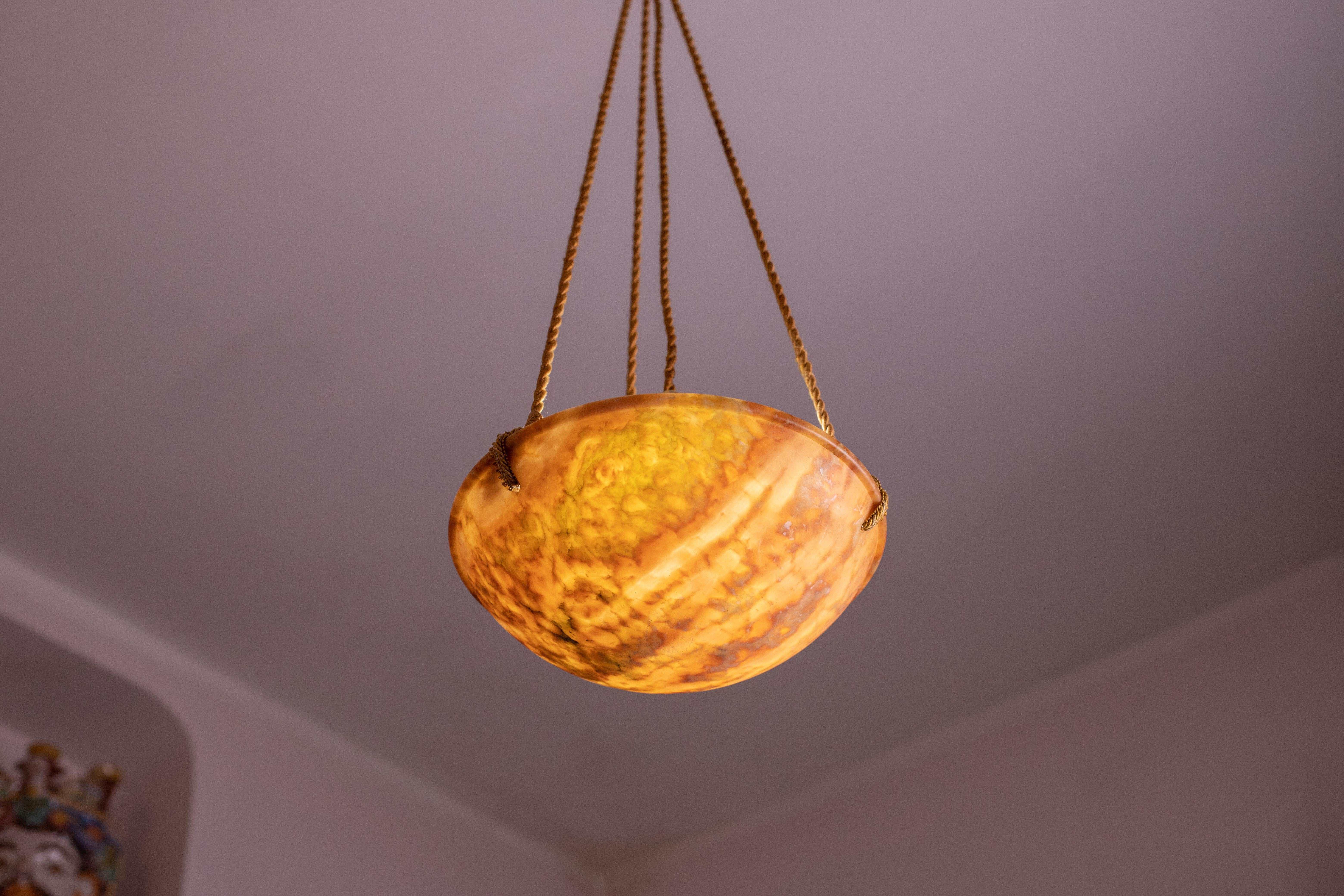 Antique Art Deco style orange alabaster hanging chandelier, circa 1950s.
A unique piece in orange alabaster, beautifully worked with shades and reflections of other colors when lit, suspended by three strings (wires). 
The light that shines through