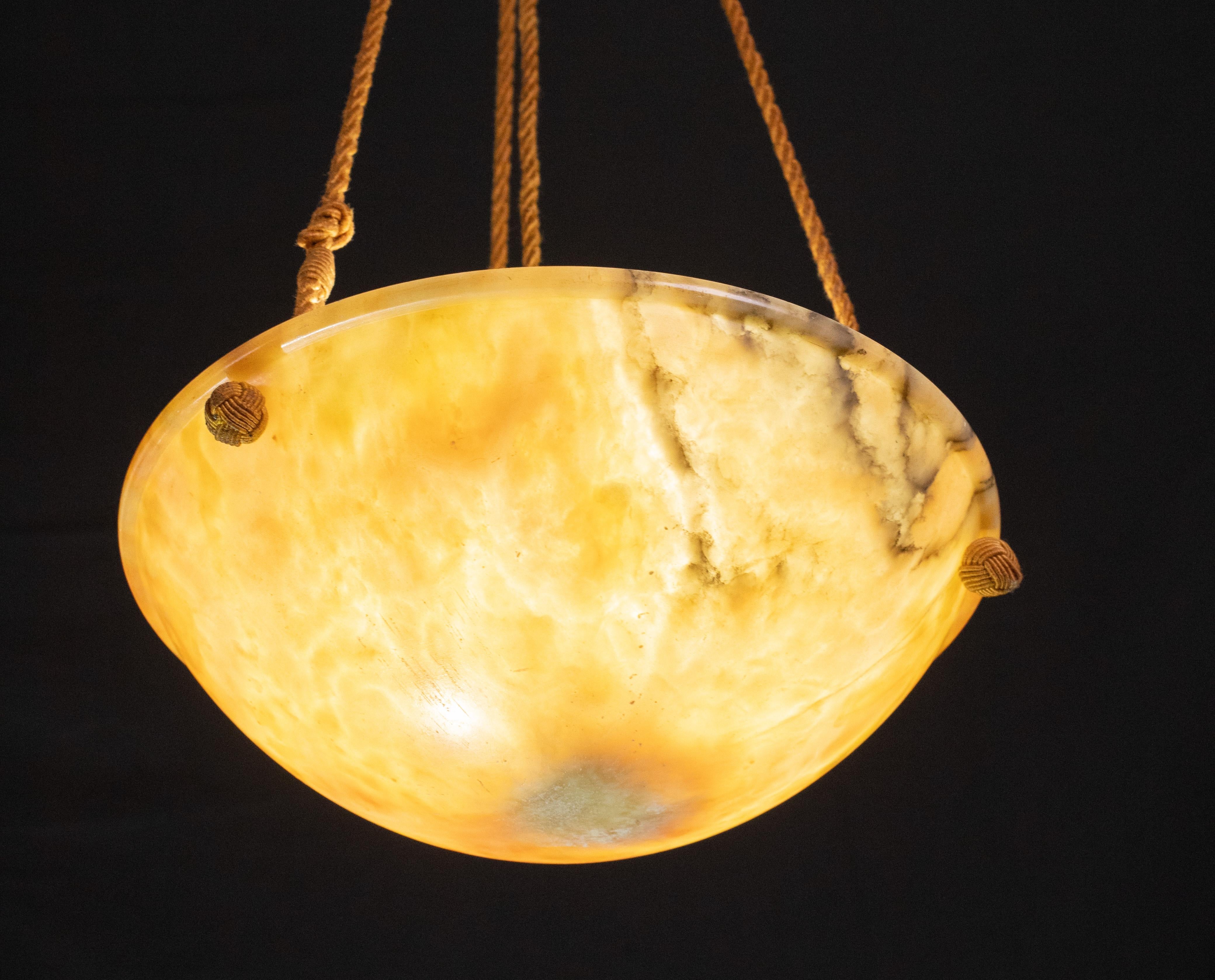 Antique orange alabaster hanging chandelier in Art Deco style, circa 1950s.
A unique piece of orange alabaster, beautifully worked with hues and reflections of other colors when lit, suspended by three strings (wires).
The light that shines through