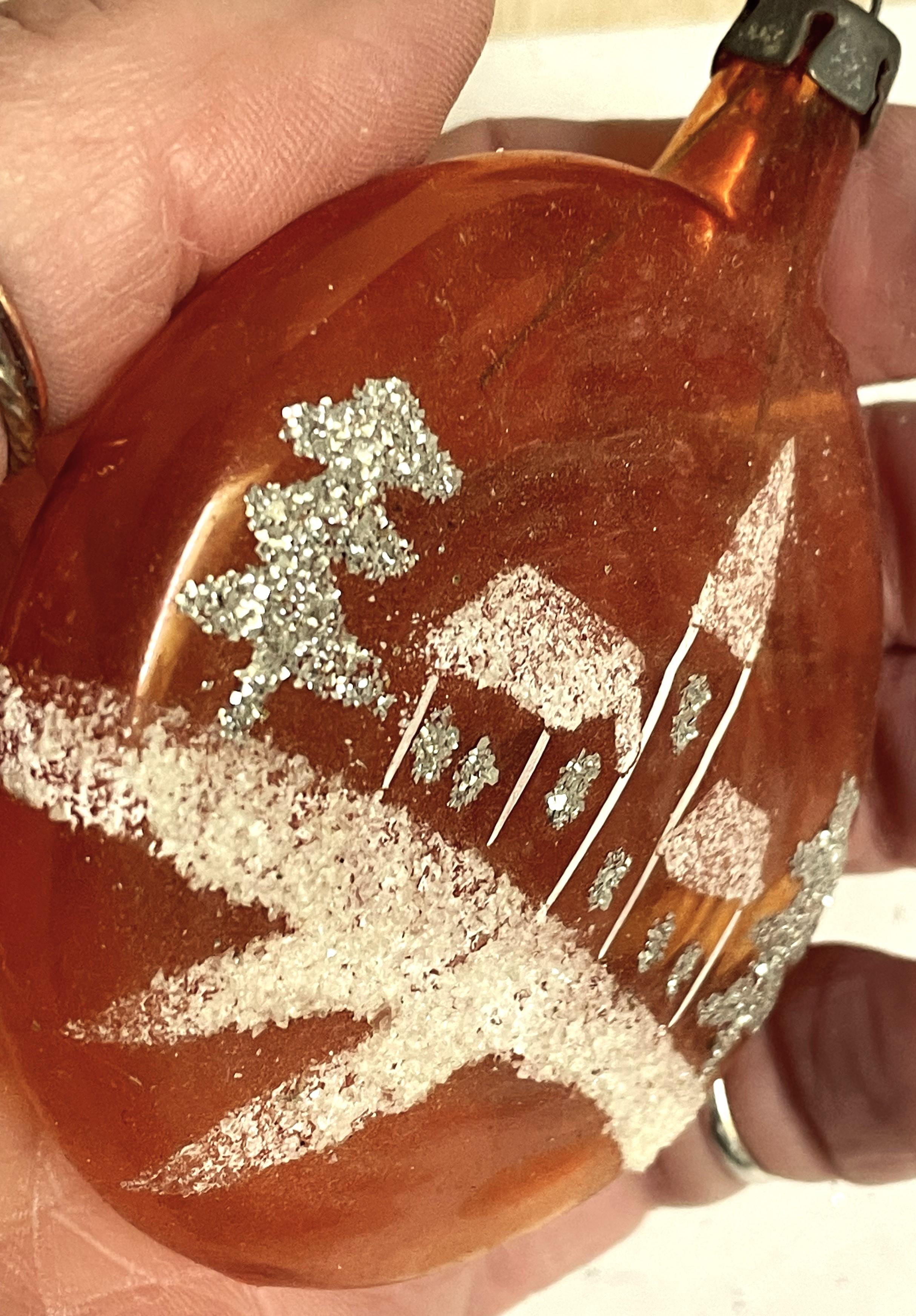 Adorabile ornamento per l'albero di Natale a palla schiacciata in vetro arancione soffiato a mano con una chiesa completa di campanile dipinta a mano sul davanti. Il terreno e i tetti coperti di neve sono glitterati di bianco, mentre le finestre e