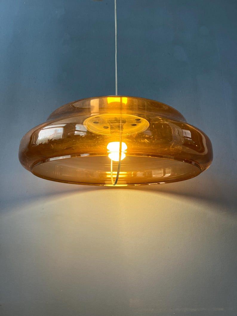Translucent flying saucer space age pendant lamp by Herda. The shade consists of acrylic glass material in orange/brown colour. The lamp requires one E27/26 lightbulb.

Additional information:
Materials: Metal, plastic
Period: 1970s
Dimensions: ø: