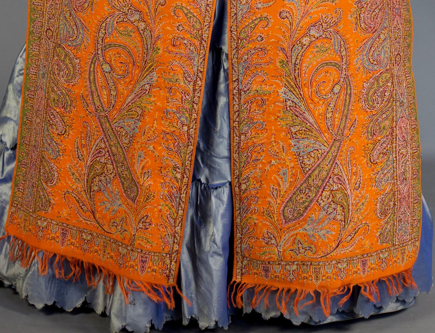 Circa 1850/1855
France
 
Rare Woven shawl with a cut-out lancet shape that adorns the shoulders of the elegant crinoline from the end of the Louis Philippe period. Lush vegetal decor loaded with wavy stems boteh rising in the bright orange central