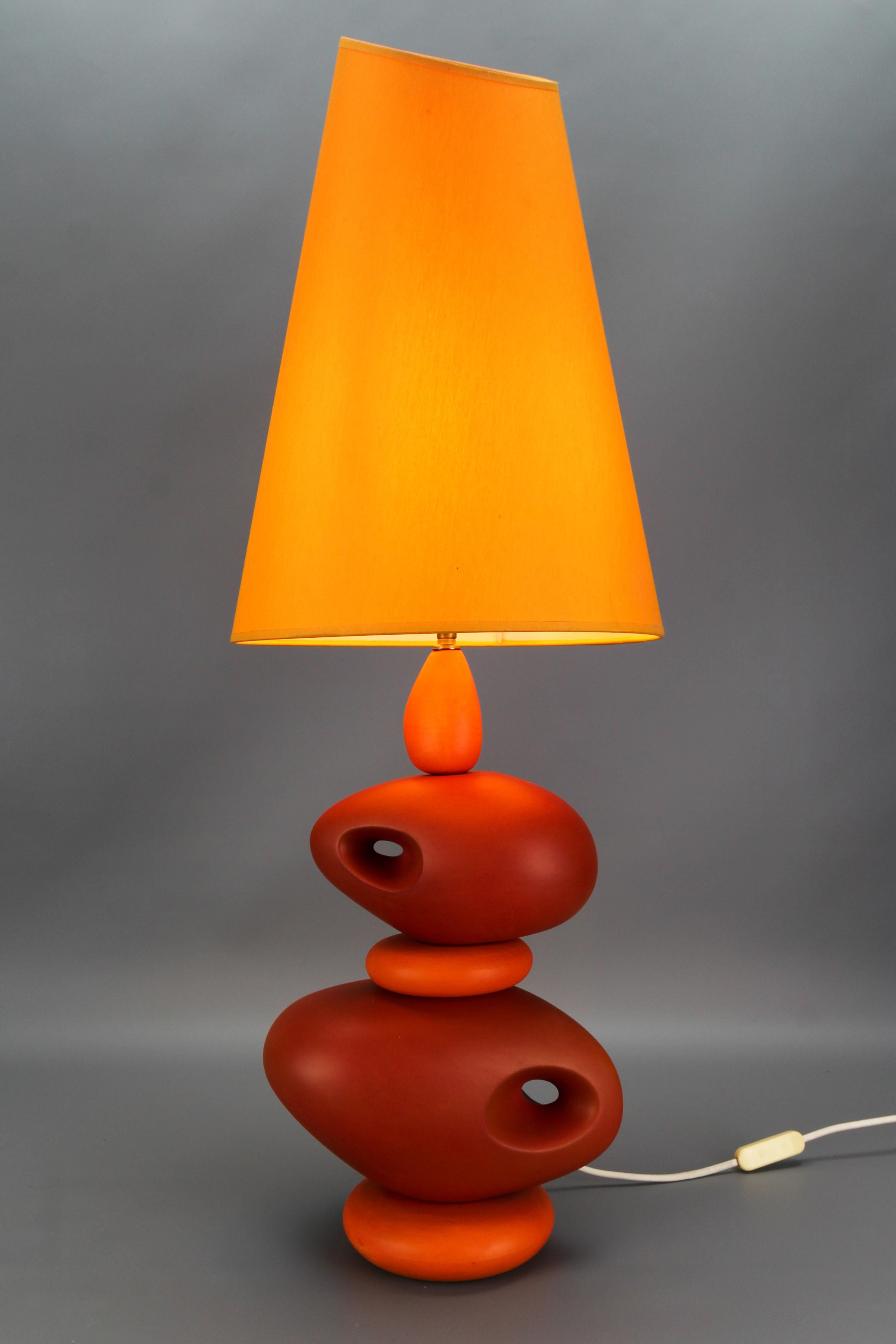 French orange ceramic table lamp by Louis Drimmer from the late 20th Century.
This colorful Post-Modern table lamp features an impressive lamp base - pebble-shaped irregularly stacked spheres made of ceramic in dark and light orange color with the