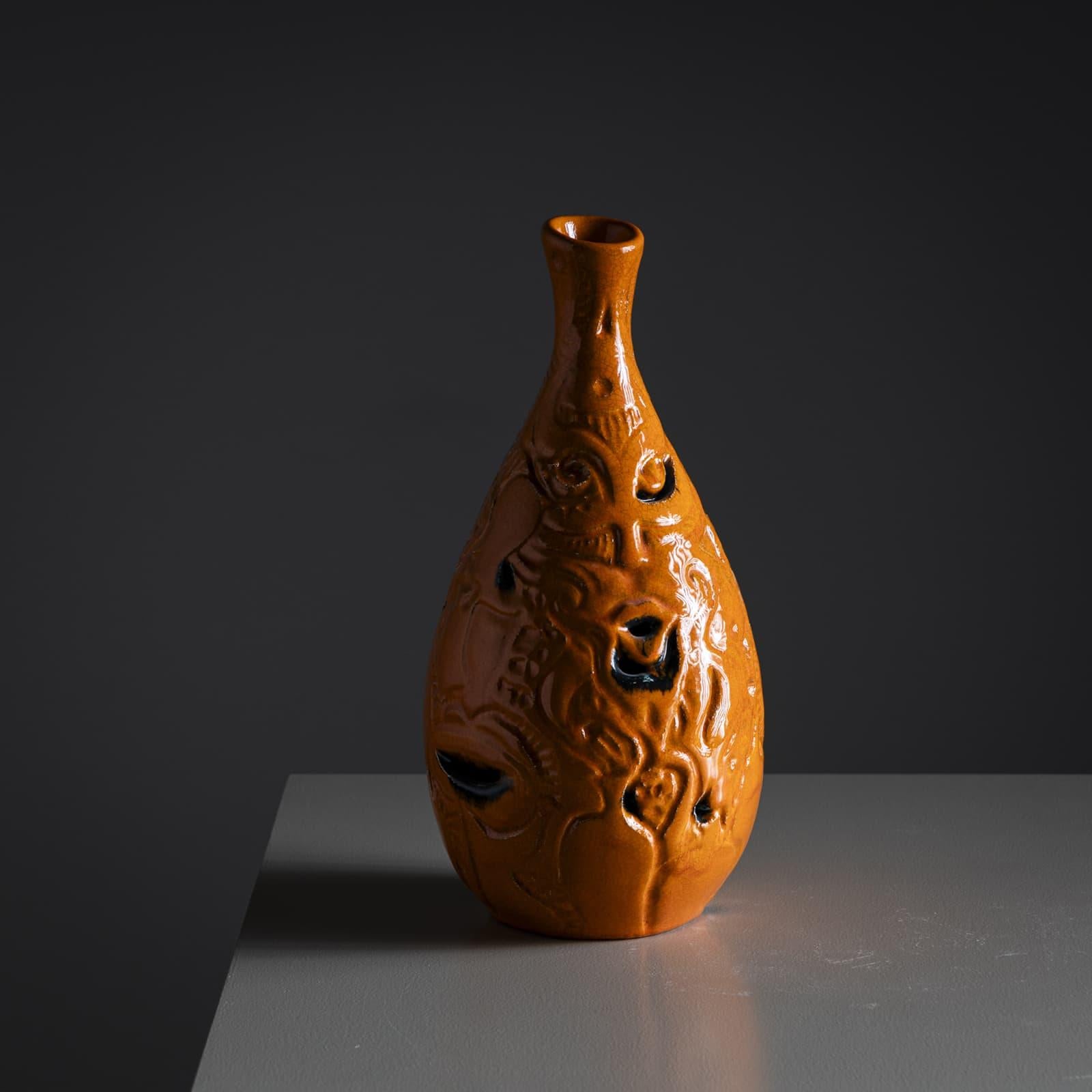 Vaso in ceramica smaltata arancione, firmato POEMU / de Mons / Aix sulla base. La parete mostra un rilievo astratto con accenti neri. Una fine craquelure ricopre l'intero vaso.  

Poemu è un artista francese multidisciplinare noto per la sua