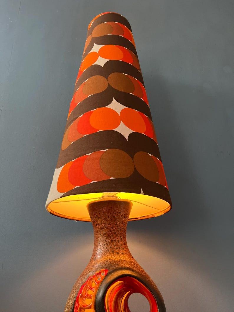 Lampadaire rouge orange west germany space age avec base en céramique et abat-jour en textile pointillé. La pièce possède deux sources lumineuses : une sous l'abat-jour et une à l'intérieur de la base en céramique. La lampe nécessite deux ampoules