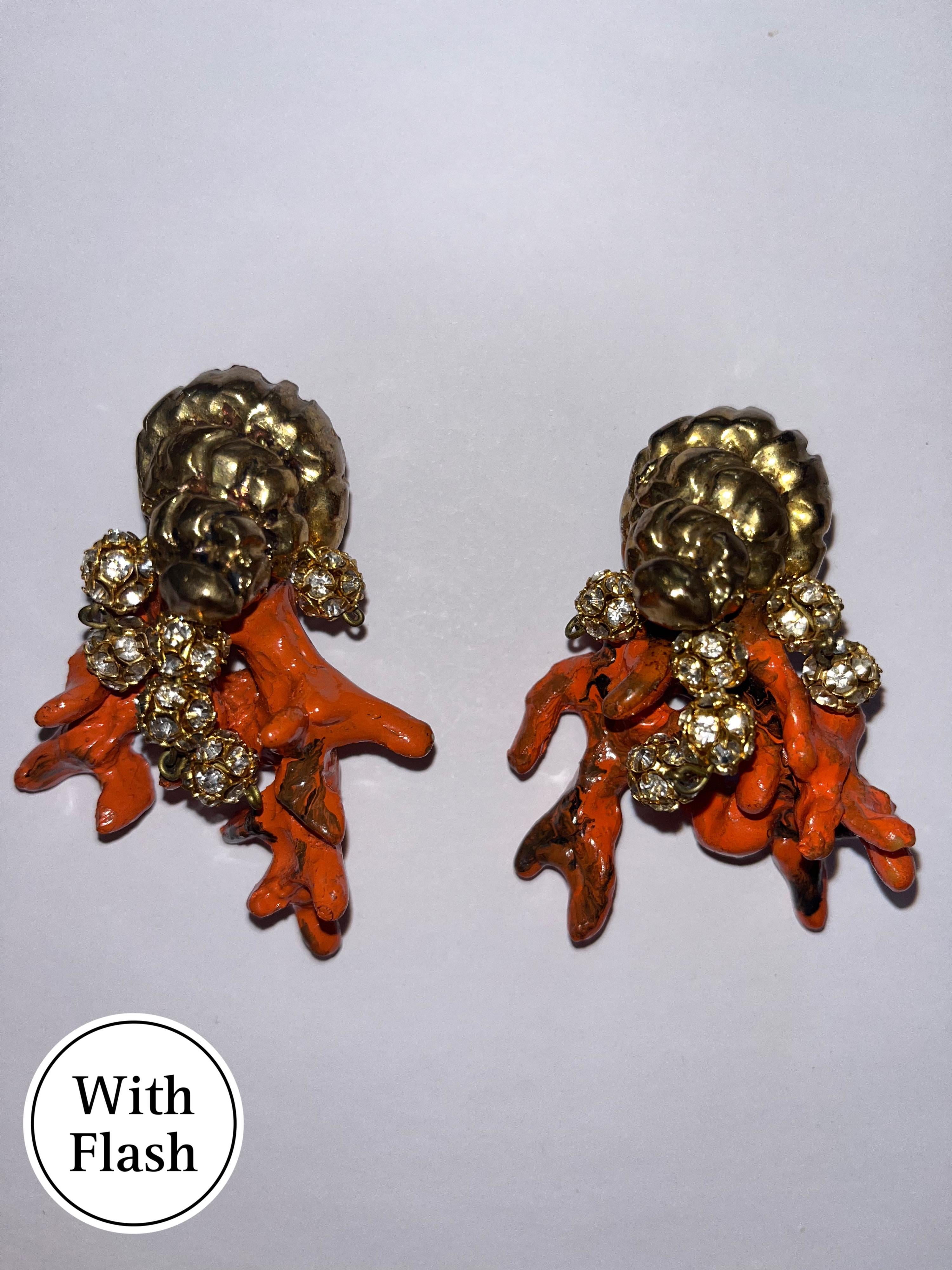 This piece of jewellery is sea-inspired clip-on earrings, combining luxurious textures with bold colours. The earrings feature a gold-tone shell motif at the top. On the inside of the clip, we see the hallmark of 