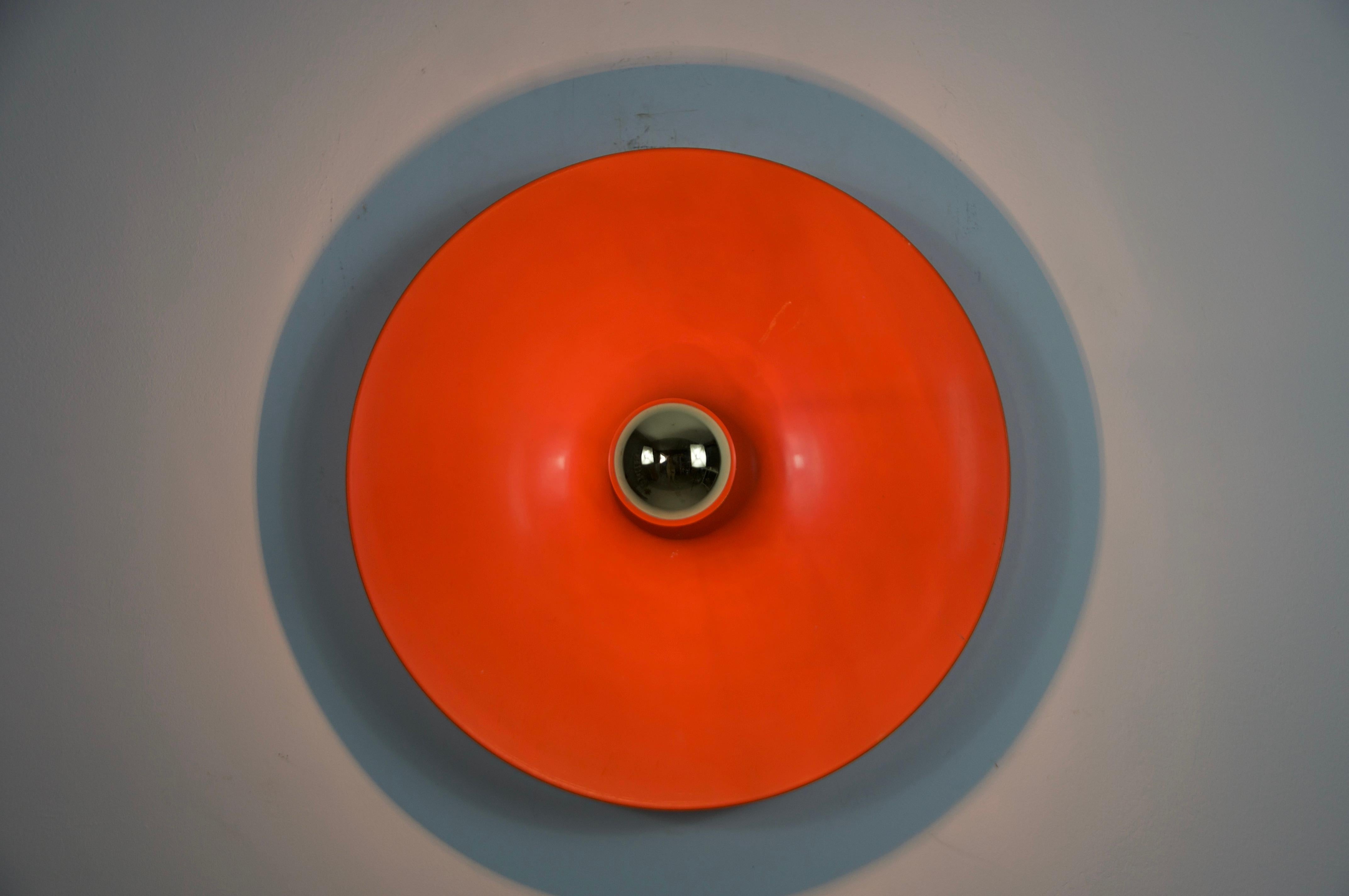 Se trata de una llamativa lámpara de pared o empotrable en forma de disco de color naranja, diseñada y fabricada por Cosack en la década de 1960. Su atrevida forma geométrica con un vibrante disco de metal lacado en naranja crea una presencia