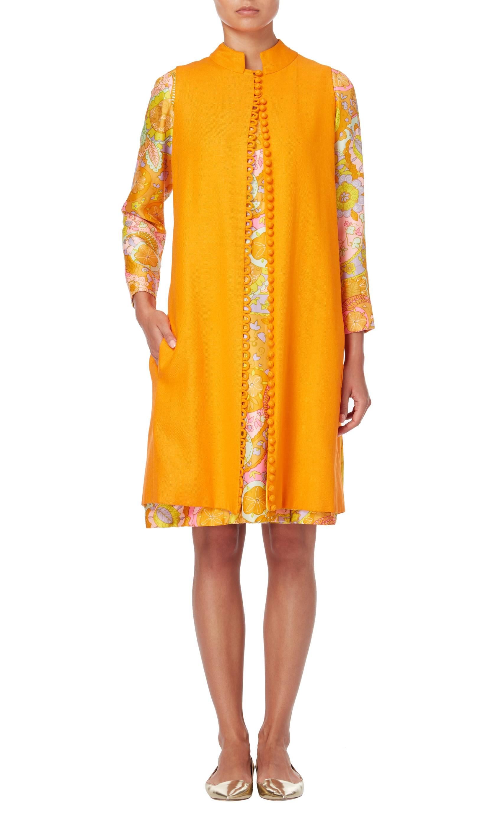 Dress and tunic ensemble by Tina Leser, circa 1973. The ensemble comprises of a floral printed dress, featuring an all-over multi-coloured floral print and an orange tunic with mandarin collar.				